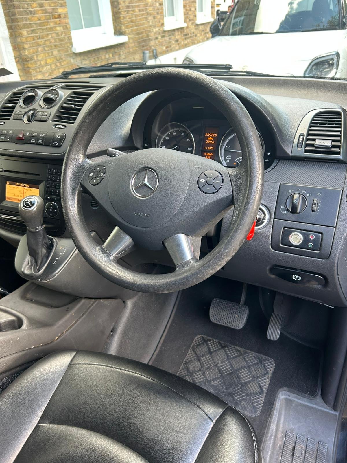 Interior view of a Mercedes-Benz vehicle dashboard showing steering wheel, instrument panel, gear shift, and other controls.