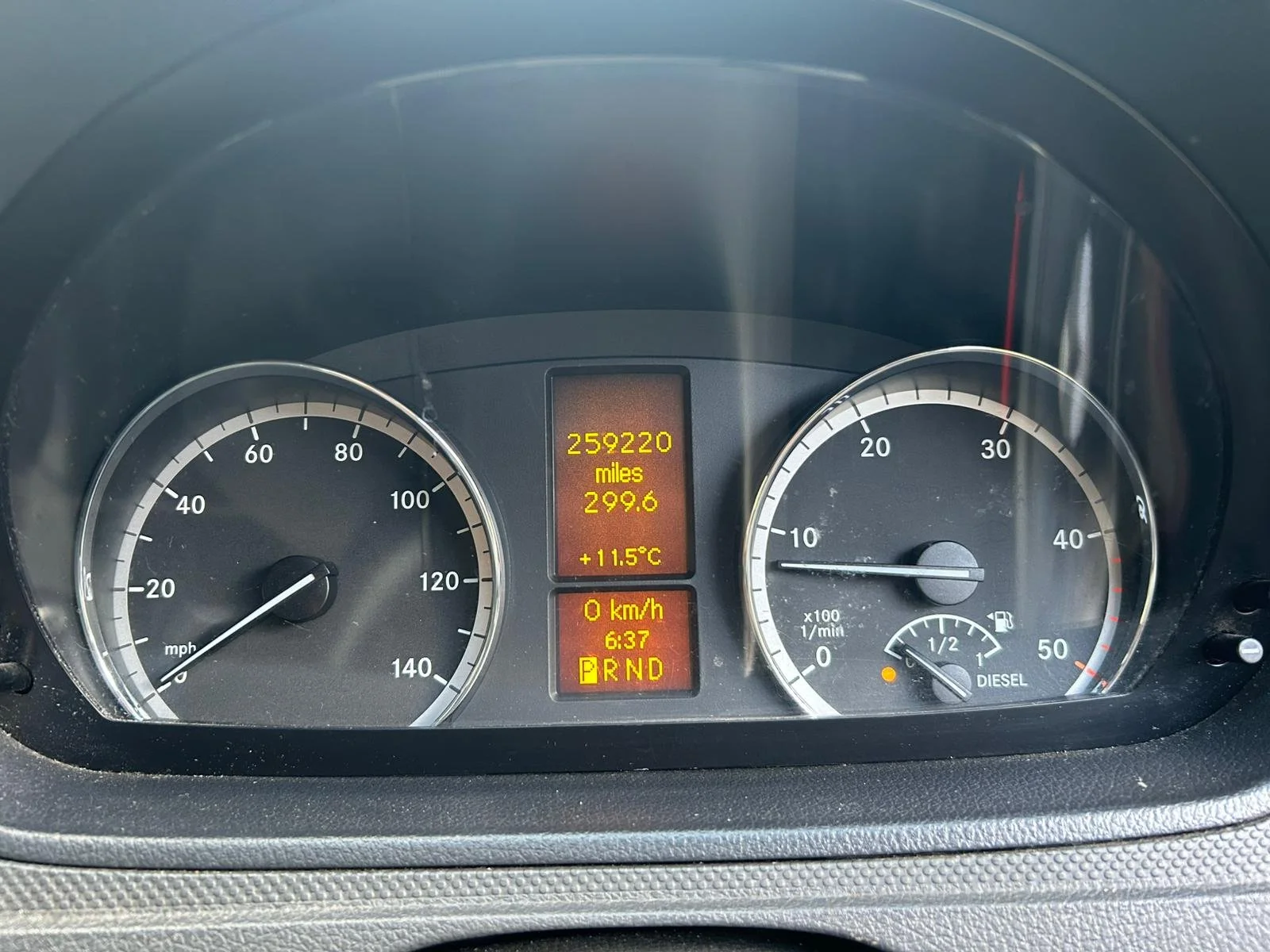 Car dashboard showing 25,920 miles driven, 299.6 miles since last reset, current temperature 11.5°C, speed 0 km/h, time 6:37, and fuel gauge indicating nearly full.
