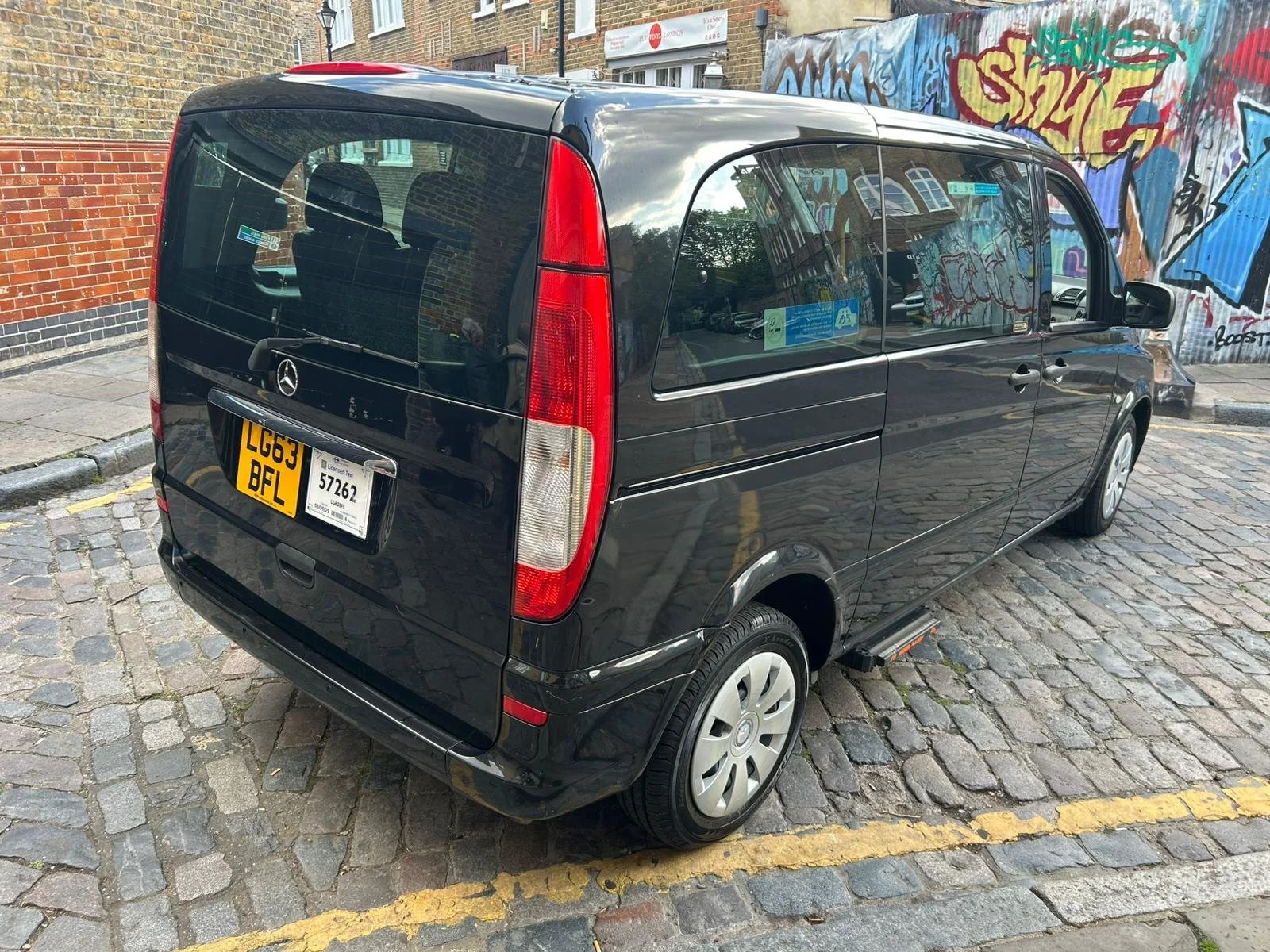 Black Mercedes-Benz van parked on cobblestone street with graffiti mural in background.