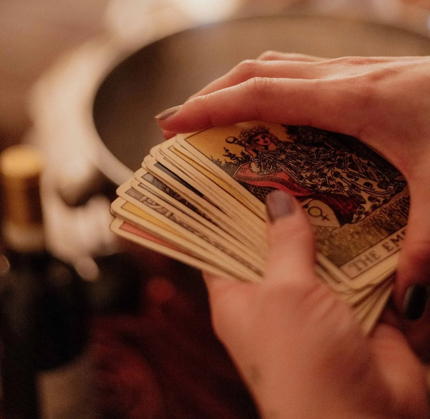 Person holding a deck of tarot cards, partially visible hand, blurred background.