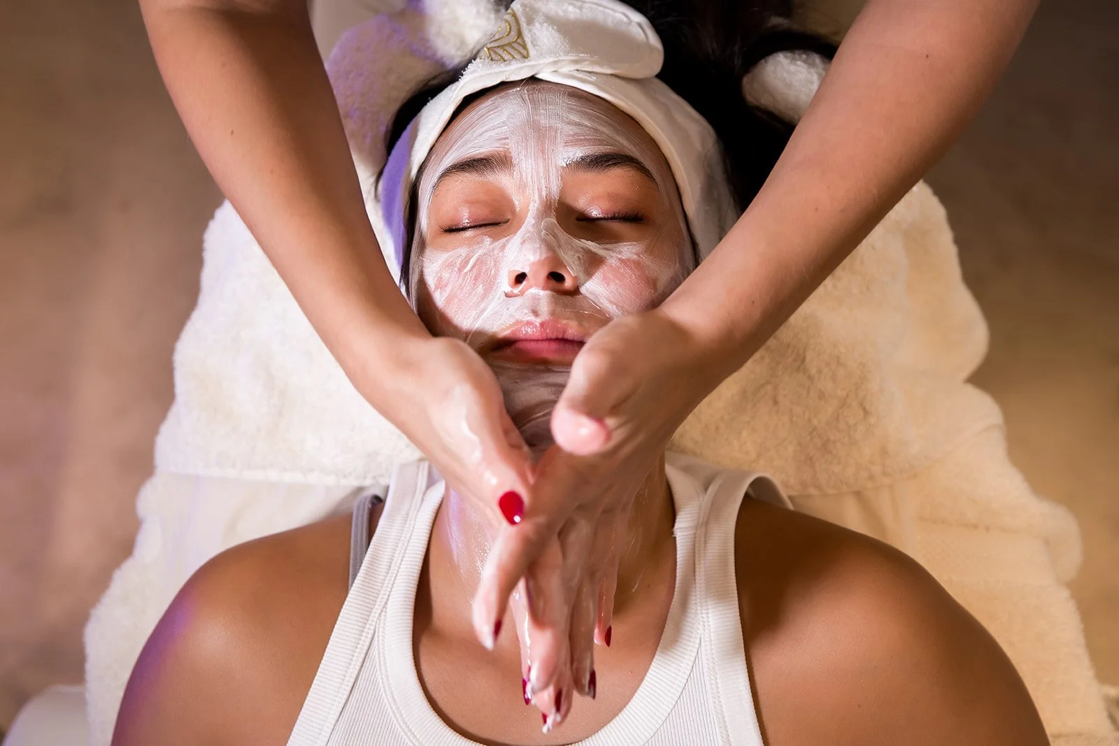 A woman with a face mask receiving a facial massage at a spa.