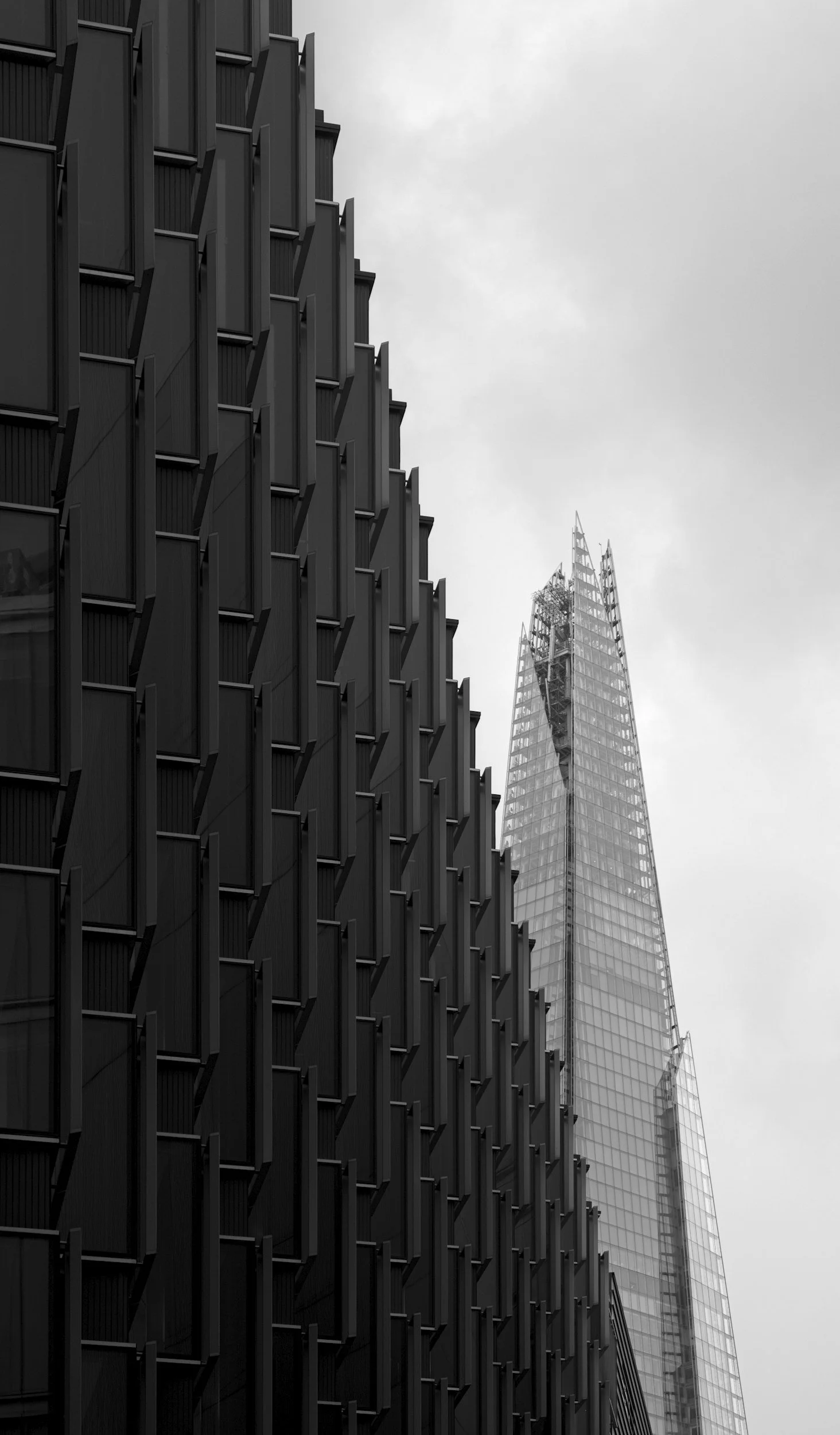 Black modern building with a textured facade next to a glass skyscraper under a cloudy sky.