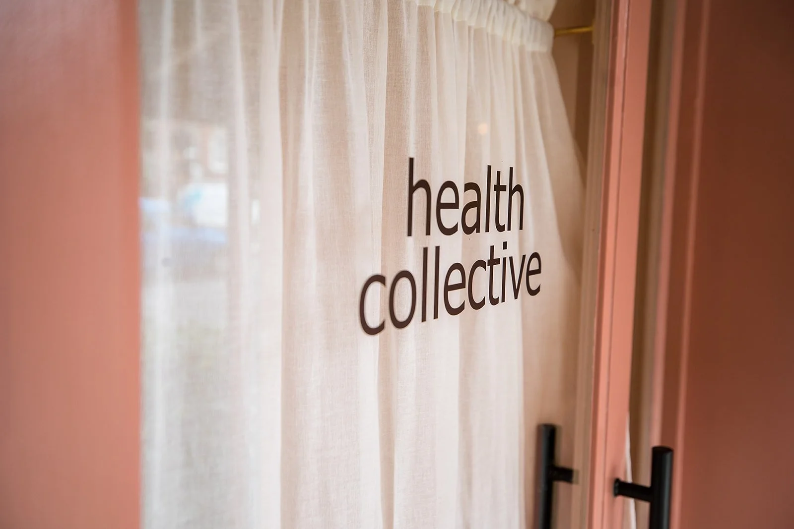 A window with light curtains and the words 'health collective' written on it in black letters.