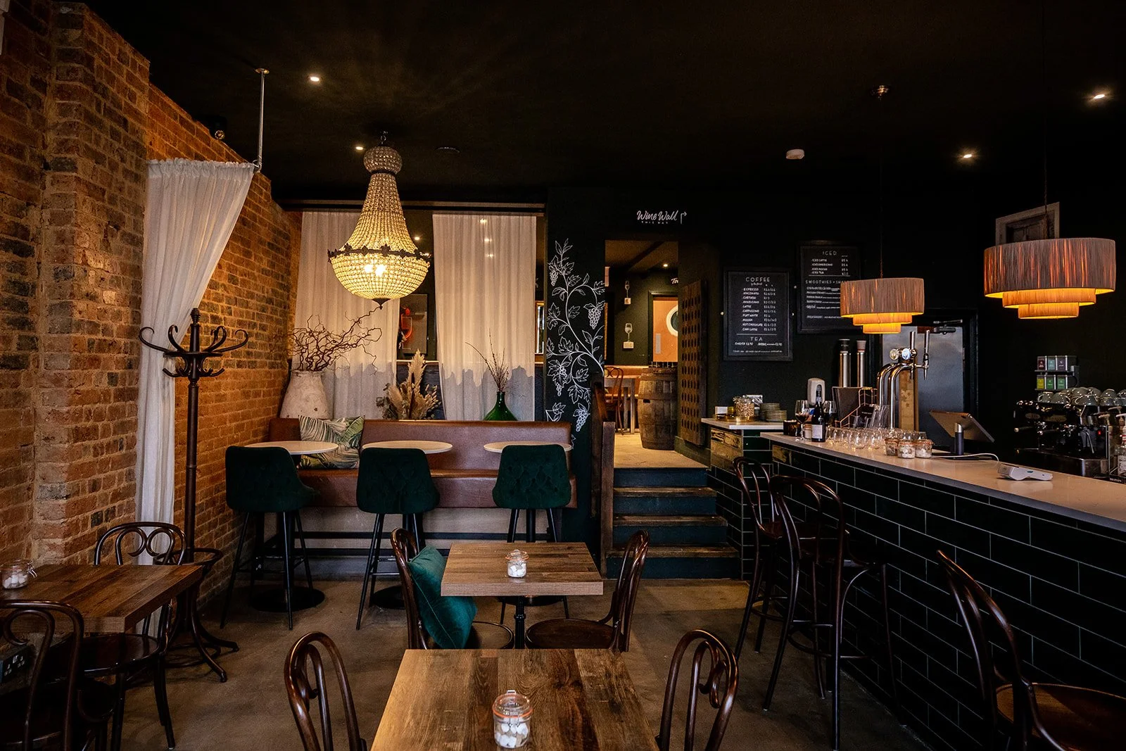 Interior of a cozy cafe with bar seating, a chandelier, brick wall, and dim lighting.