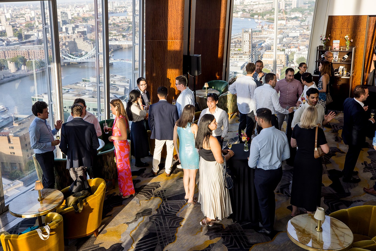 A group of people socializing at a rooftop cocktail party with city skyline and river views in the background.