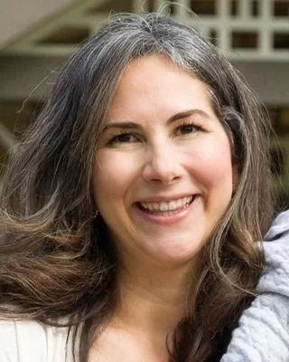 A woman with long, wavy hair smiling outdoors.