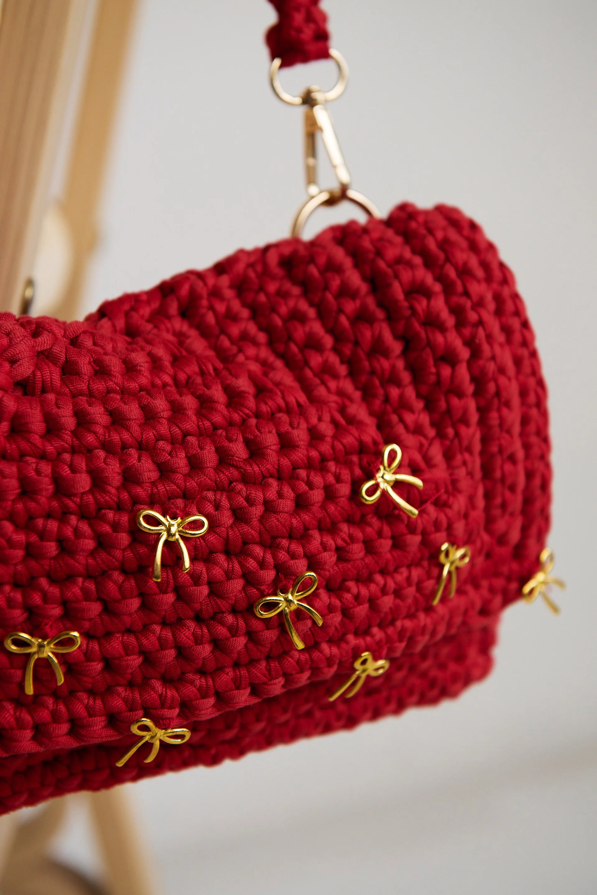 Close-up of a red, knitted handbag with small golden bow-shaped embellishments.