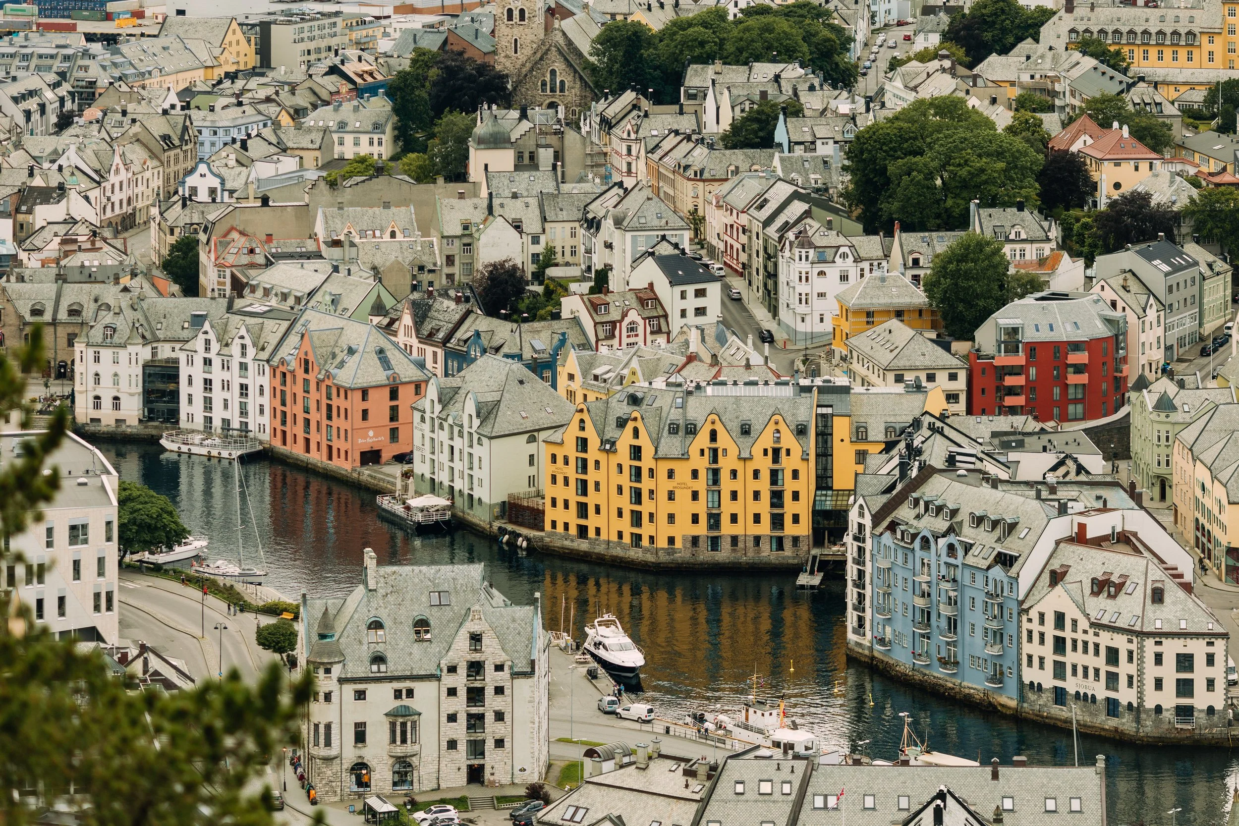 Overblikk av en by med fargede bygninger ved en kanal med båter og grøntområder.