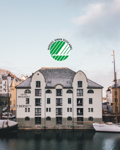 Fasade av et gammelt bygg ved vannet med en Nordisk Swan Ecolabel-logo over.