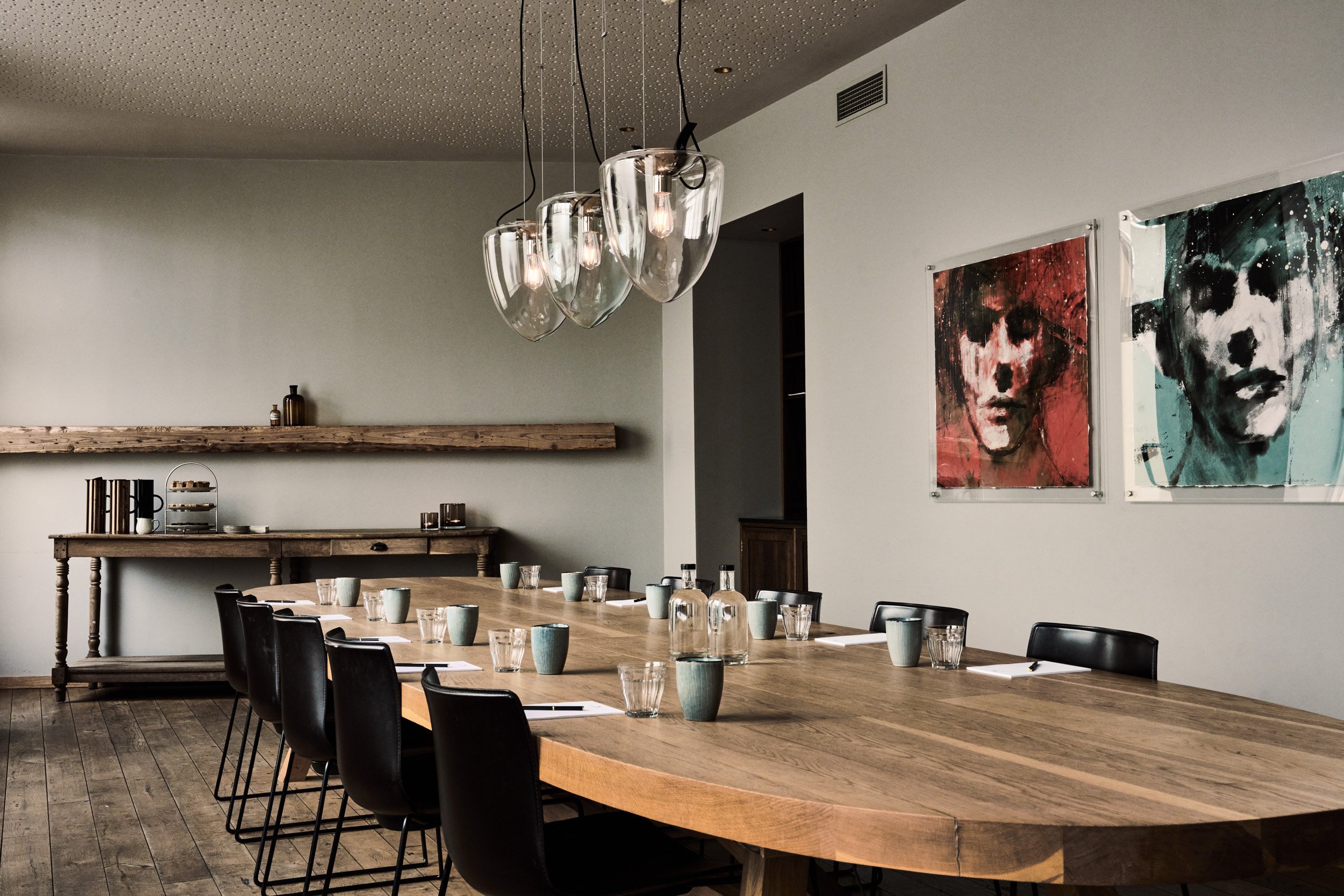 Et bord dekket med kopper og glass i et rom med kunstverk på veggene og en unik lysekrone i taket.