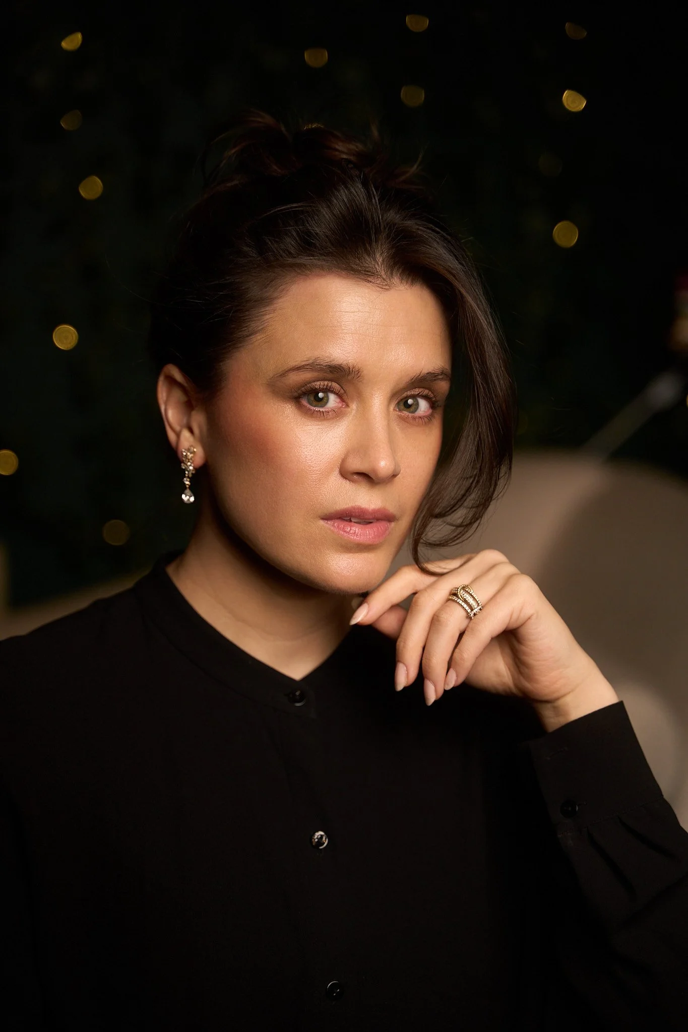 Ramona Mallory, Broadway Actress and mentor, a woman with brown hair styled in an updo, wearing earrings and a ring, dressed in a black top, posing indoors with a blurred background of lights.