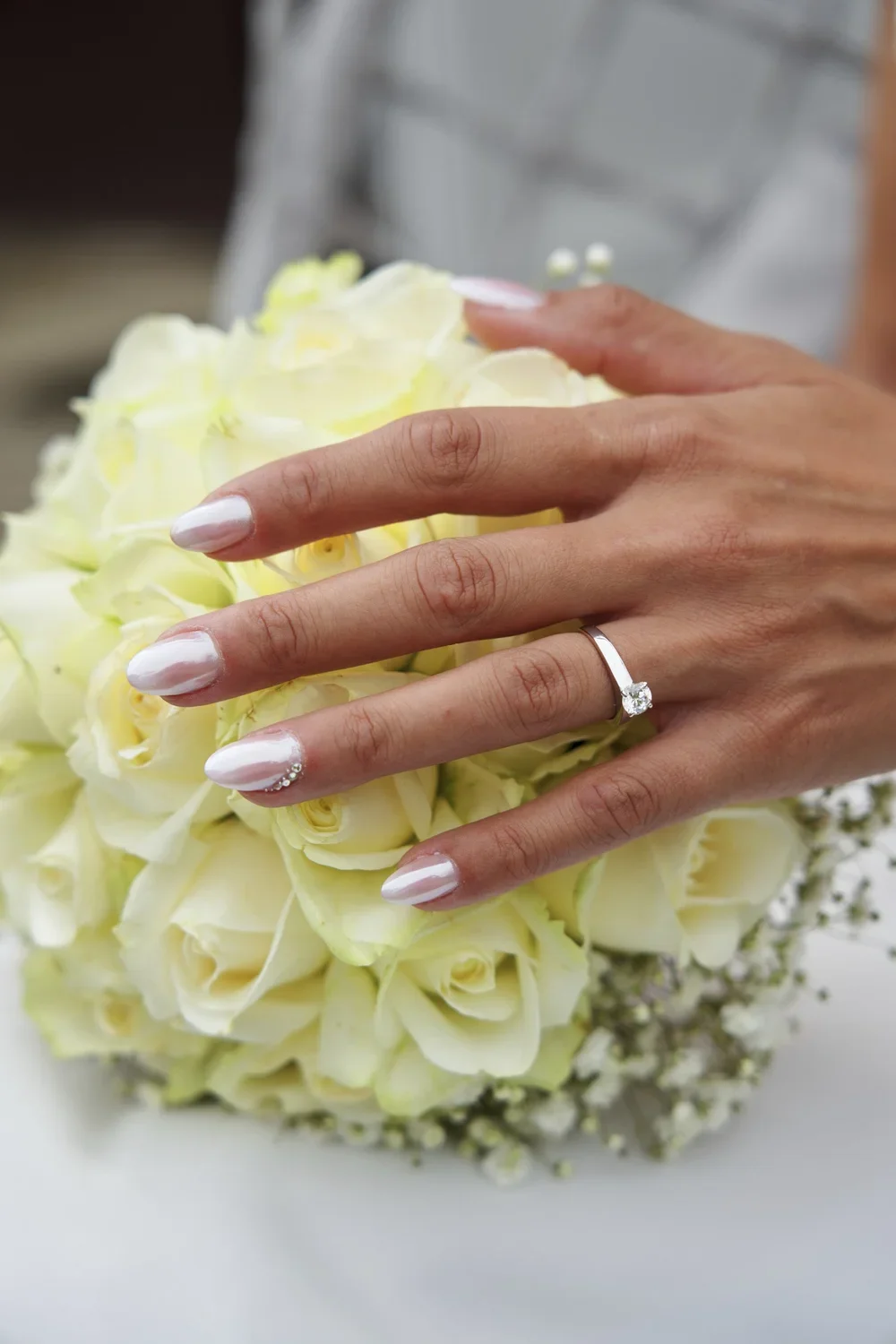 A woman's hand with a wedding ring, showing manicured nails, resting on a bouquet of white roses.