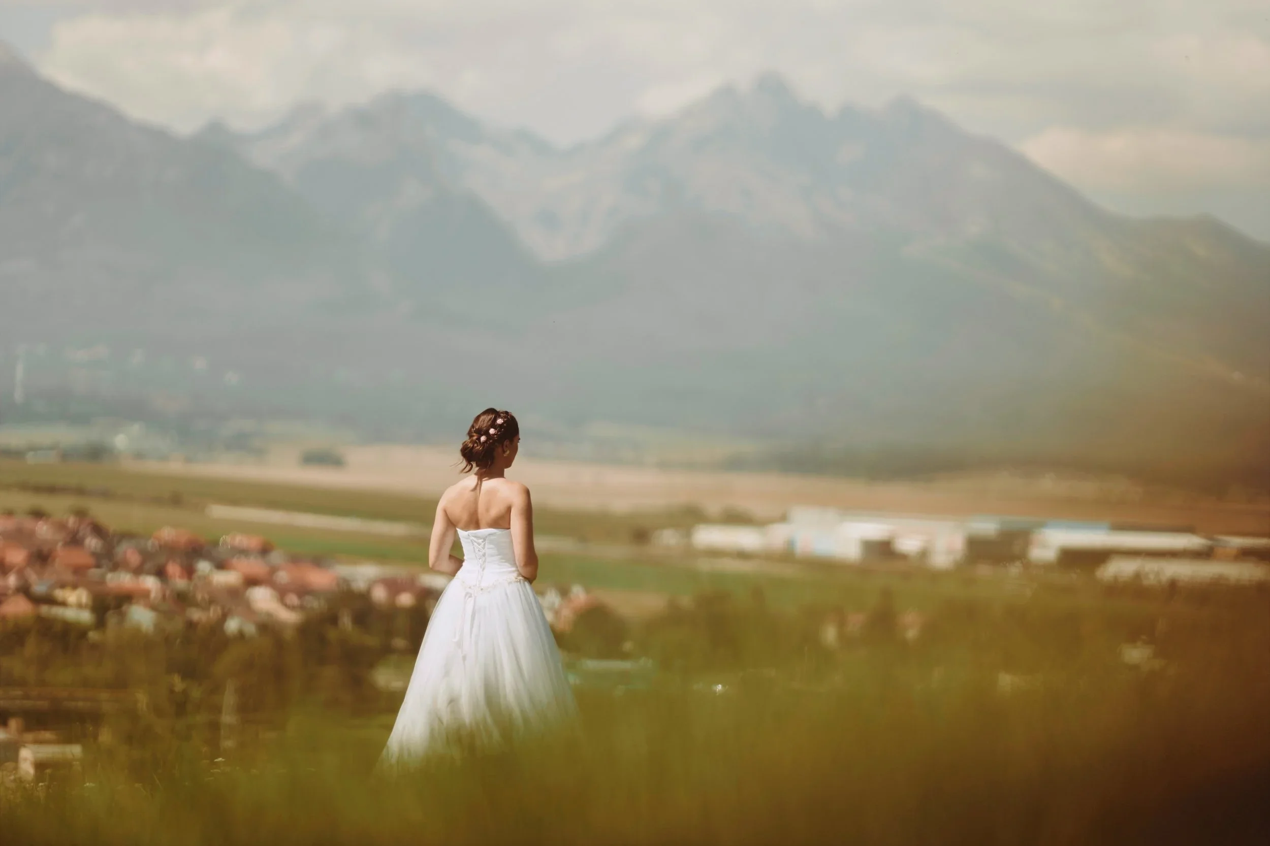 A woman in a white dress standing outdoors with a city and mountain landscape in the background.