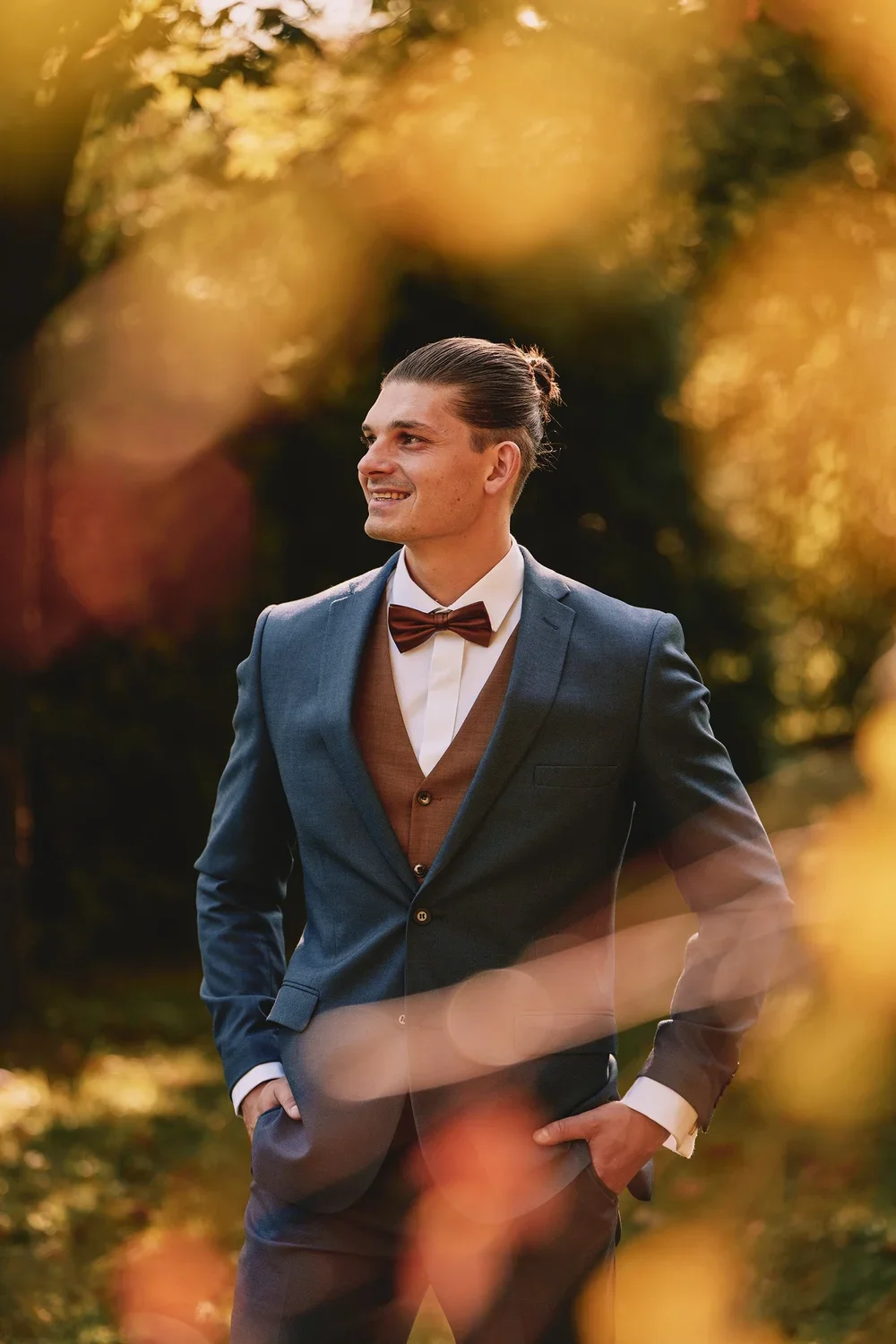 Svadobný portrét ženícha: Elegantný muž v modrom obleku so štýlovými doplnkami pózuje vonku v prírode pred rozostreným pozadím počas svadobného fotenia na Slovensku.