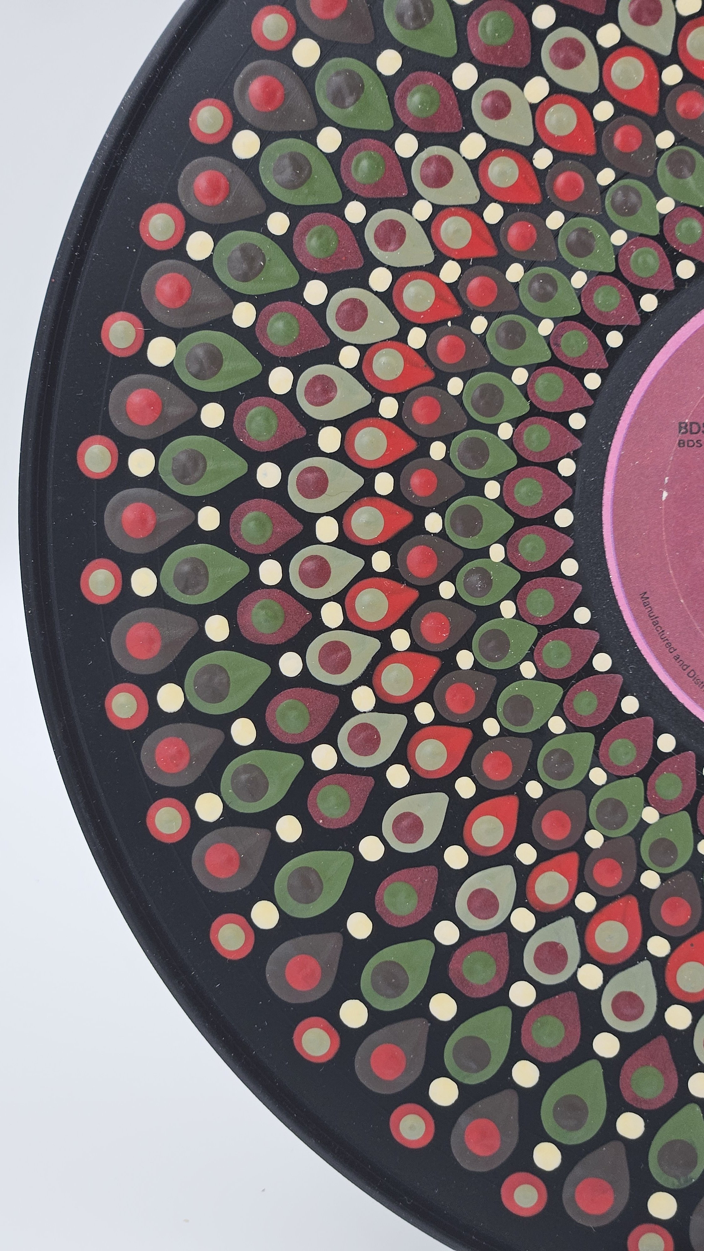 Close-up of hand-painted teardrop and dot patterns in red, burgundy, olive green, cream, and charcoal on a black vinyl record.