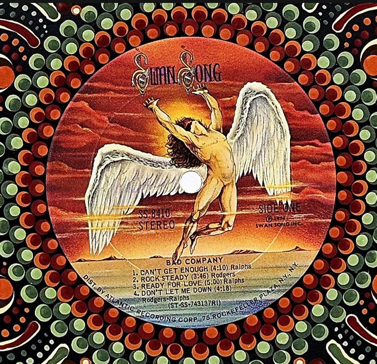 Close-up of the original Swan Song record label on Bad Company's 1974 debut album, featuring the iconic winged figure surrounded by hand-painted orange, red, and green mandala details.