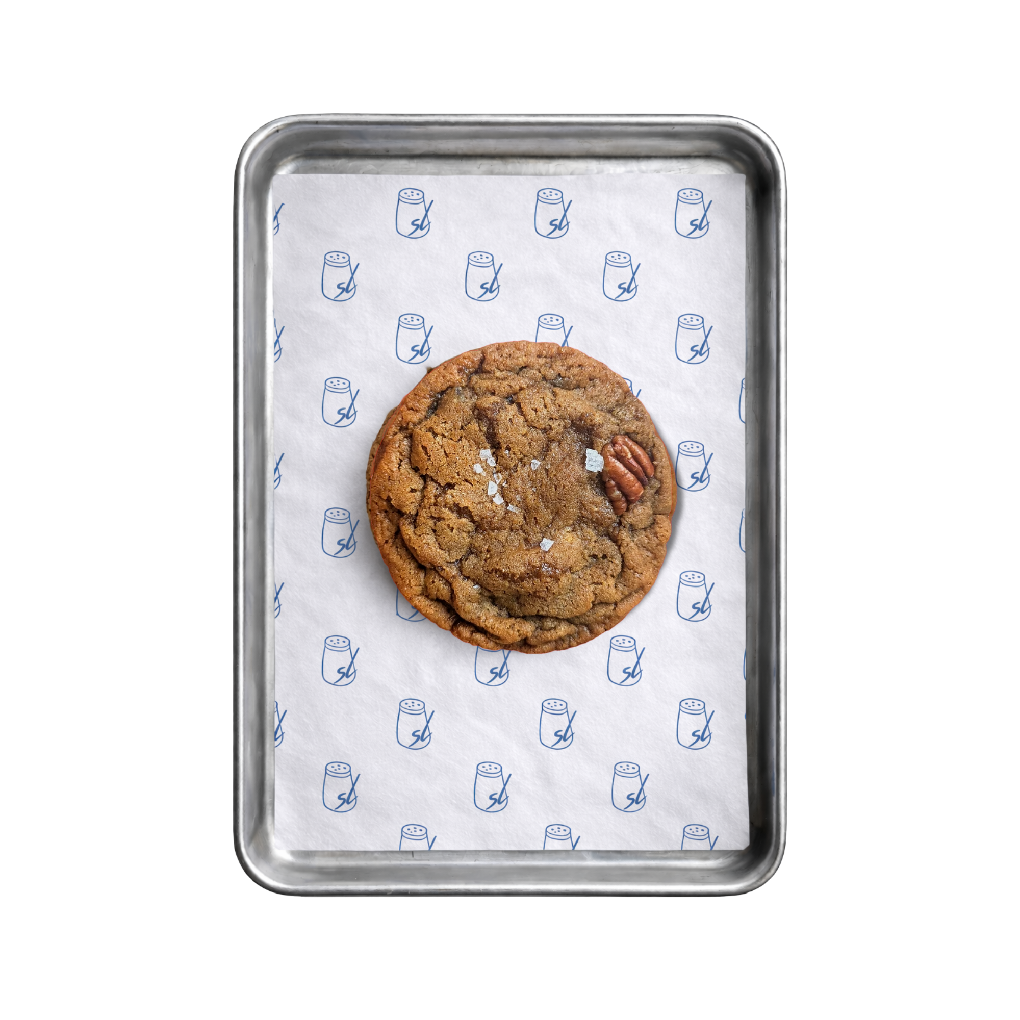Close-up of a metal tray with a sheet of white paper featuring small salt shakers printed in blue. A large pecan and stem ginger cookie is visible in the middle of the tray.
