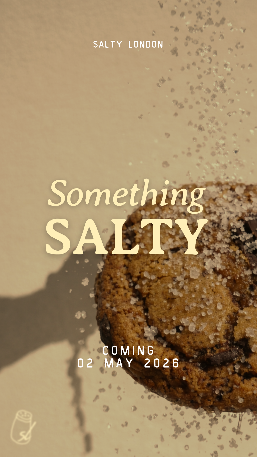 Close-up of a salted cookie with coarse salt on top, with promotional text for a product called 'Something Salty', scheduled to be released on May 2, 2026.