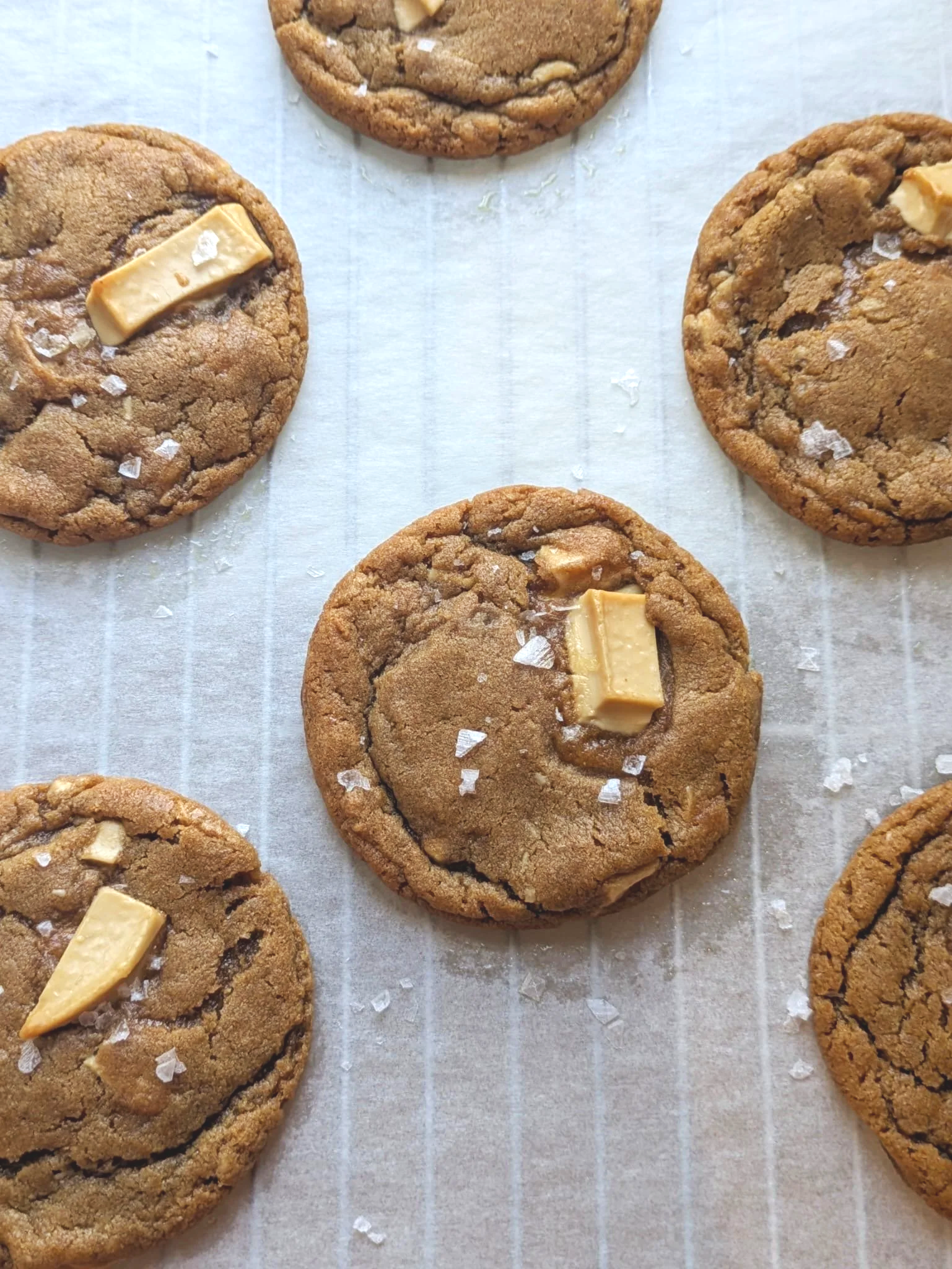 Close-up of freshly baked chocolate chip cookies topped with sea salt, arranged on parchment paper.