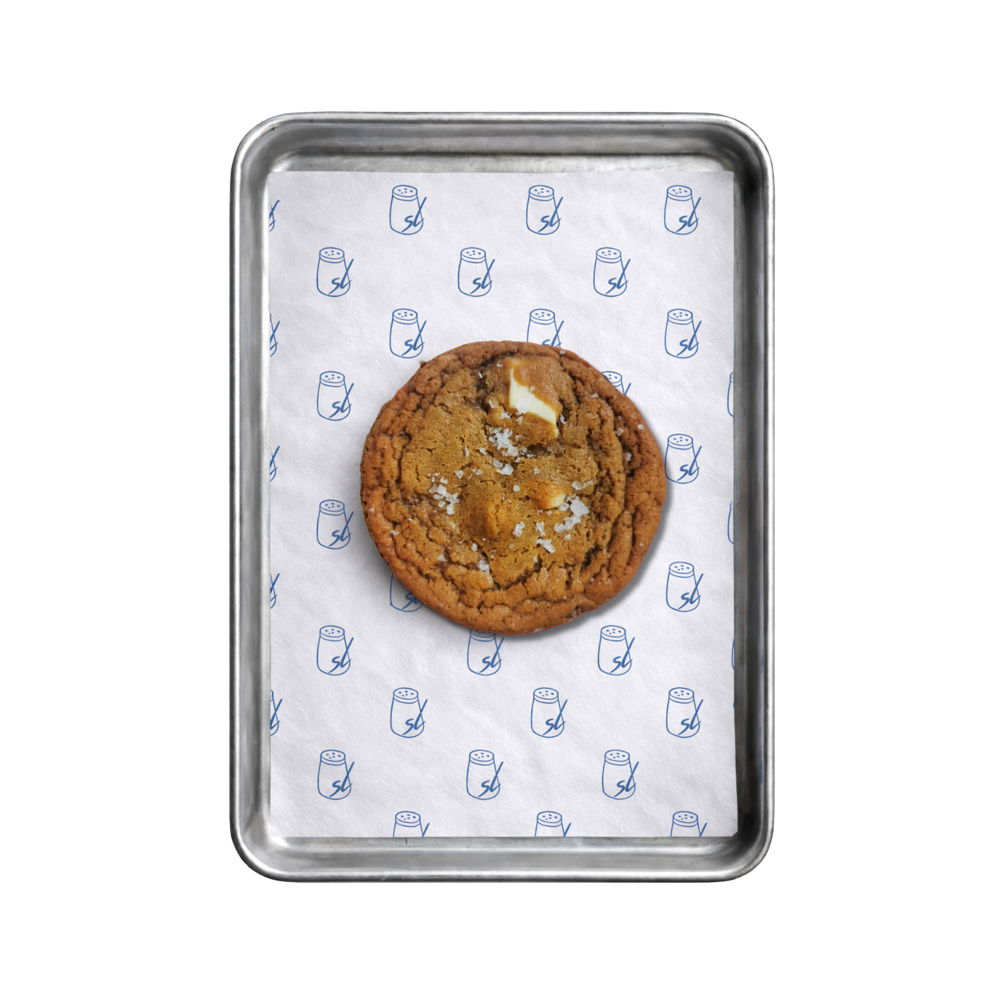 Close-up of a metal tray with a sheet of white paper featuring small salt shakers printed in blue. A large white chocolate chip cookie is visible in the middle of the tray.