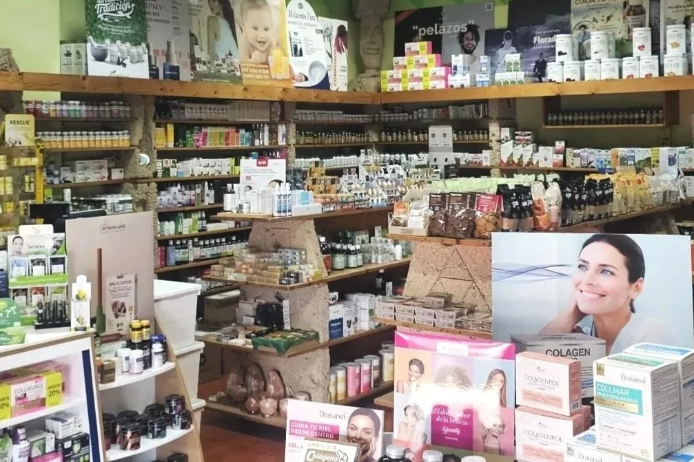 Interior de una farmacia con estanterías llenas de productos de cuidado personal, suplementos y medicamentos, y una mujer en una publicidad mostrando una sonrisa.