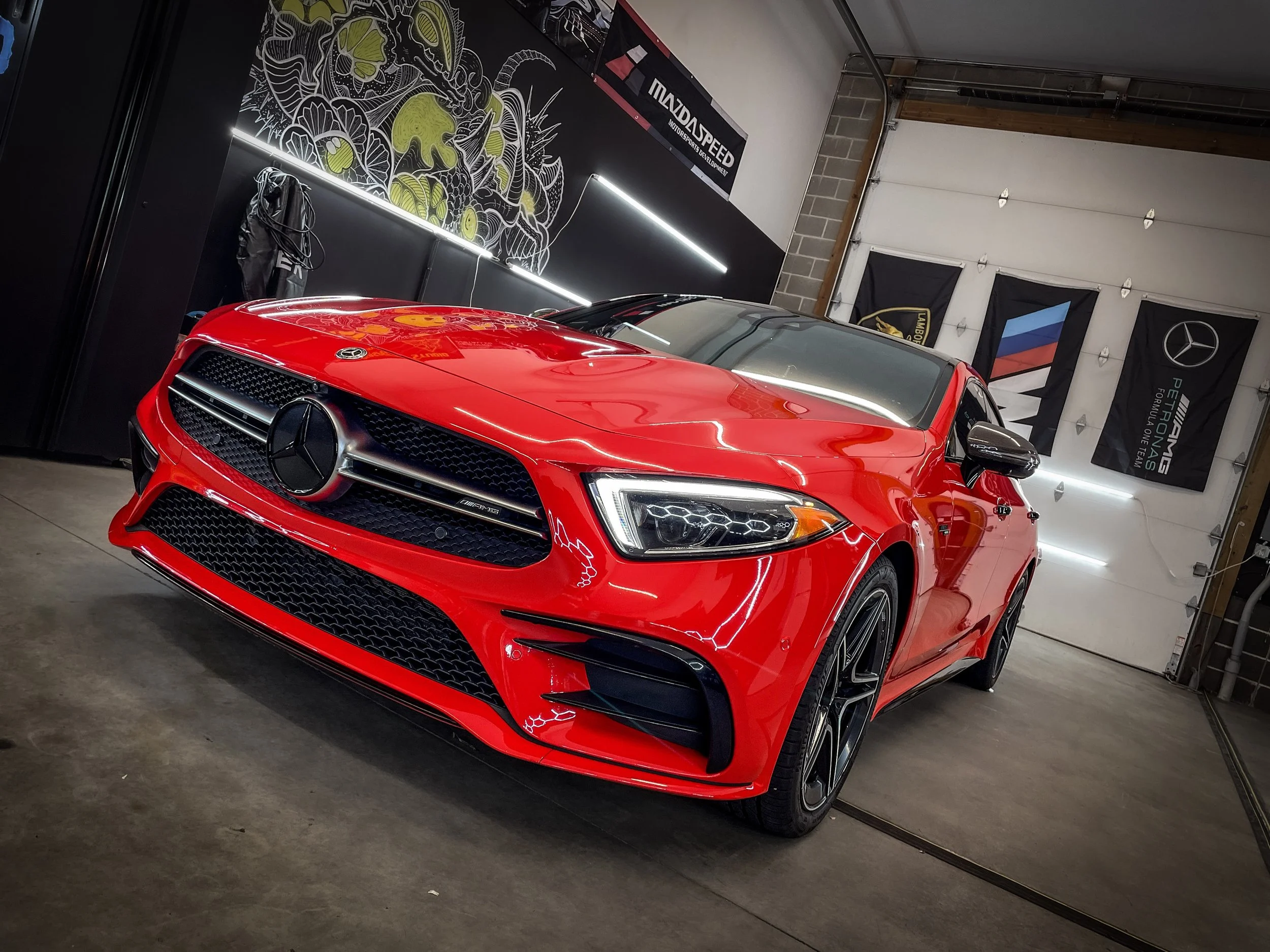 Red Mercedes-Benz car parked inside a garage with racing banners on the wall.