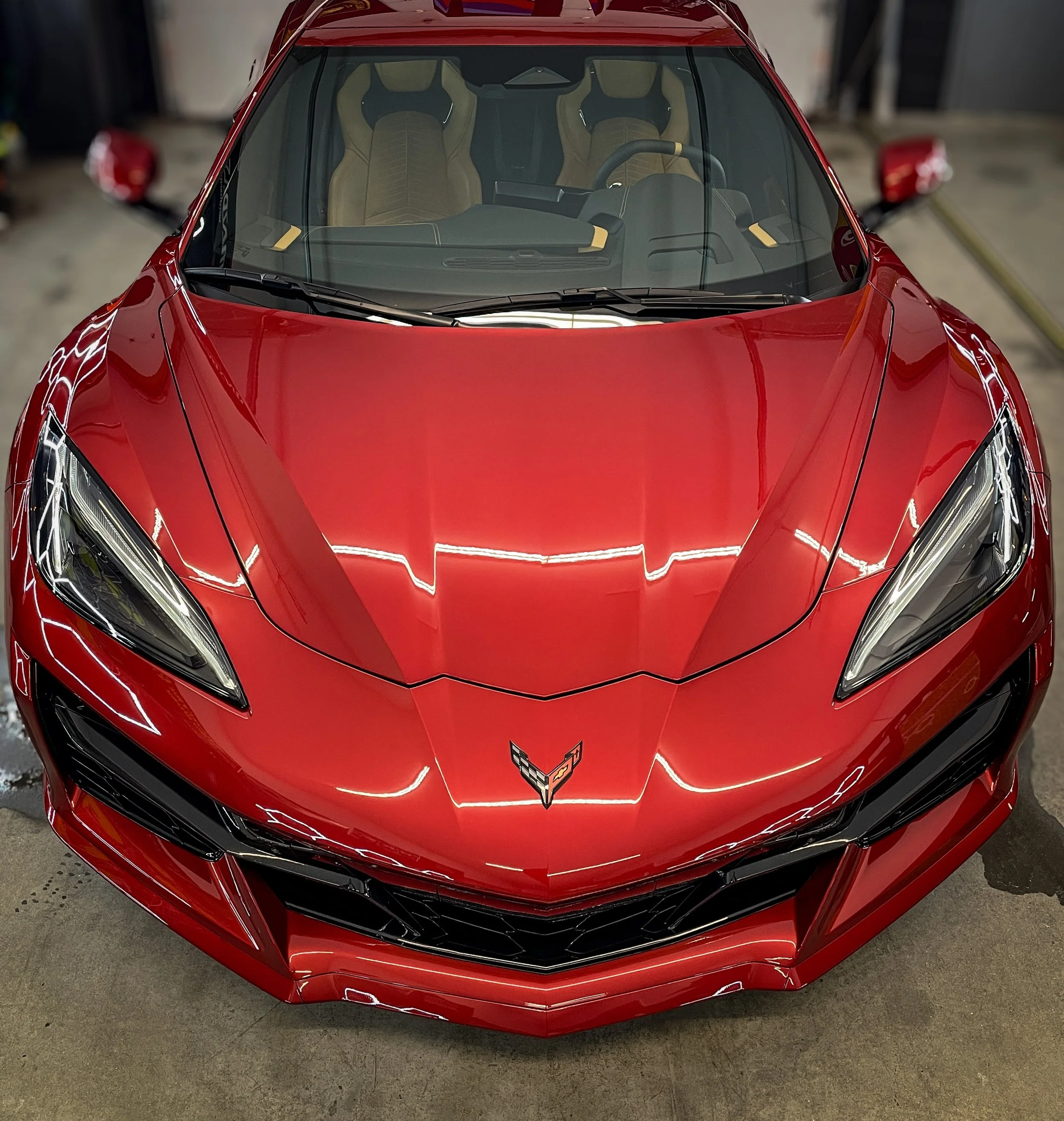 Front view of a red sports car with a sleek design, sharp headlights, and a distinctive Chevrolet Corvette emblem on the hood.