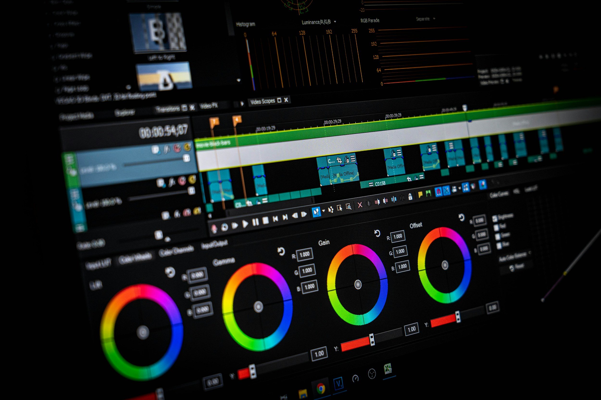 Close-up of a computer screen displaying photo editing software with color wheels, video timelines, and color correction tools.