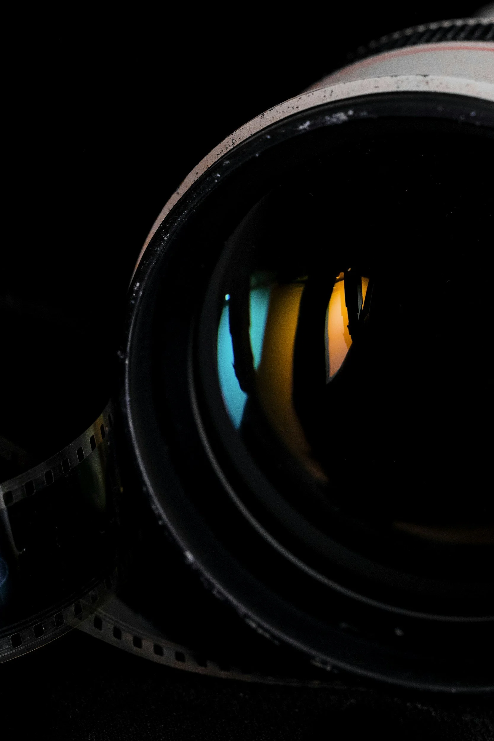 Close-up of a camera lens with reflective glass showing a colorful reflection, set against a black background.