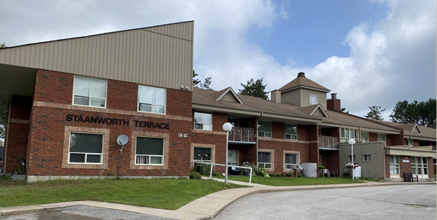 Exterior view of a brick apartment complex with balconies, satellite dishes, and a sign reading 'Staanworth Terrace'.