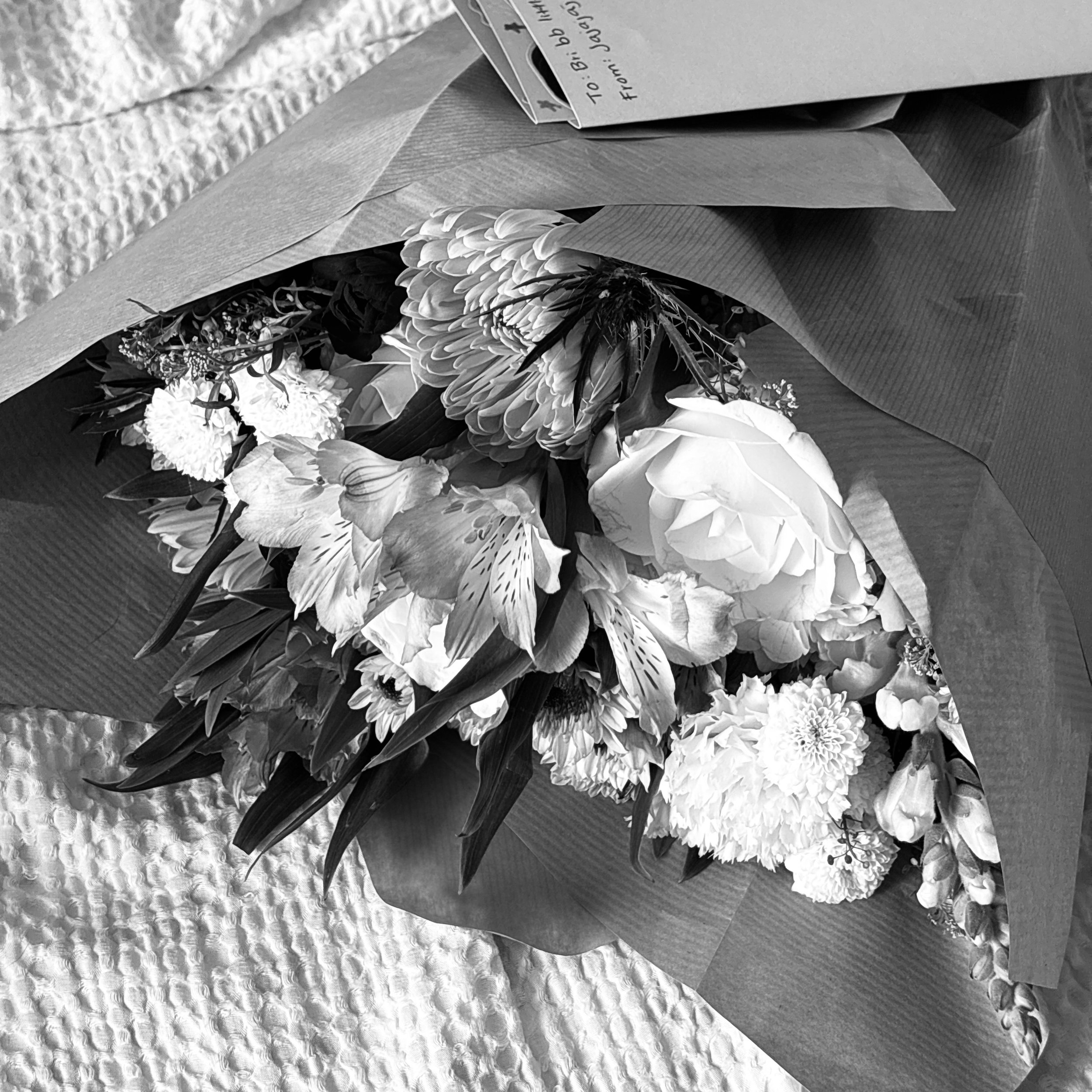 A bouquet of various flowers wrapped in paper, positioned on a textured table surface.