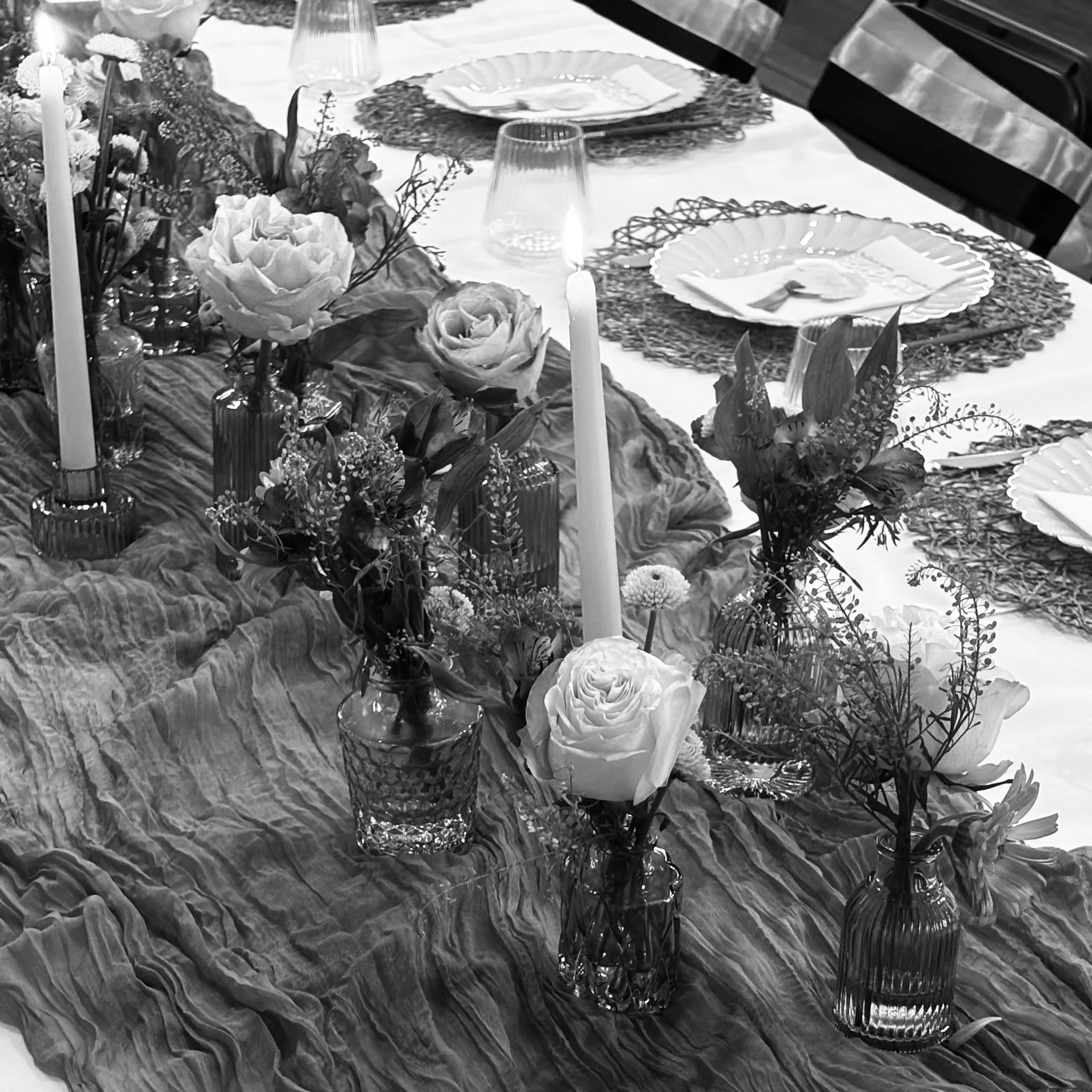 A decorated dining table with floral arrangements, candles, and tableware including plates, glasses, and napkins, set for a special occasion.