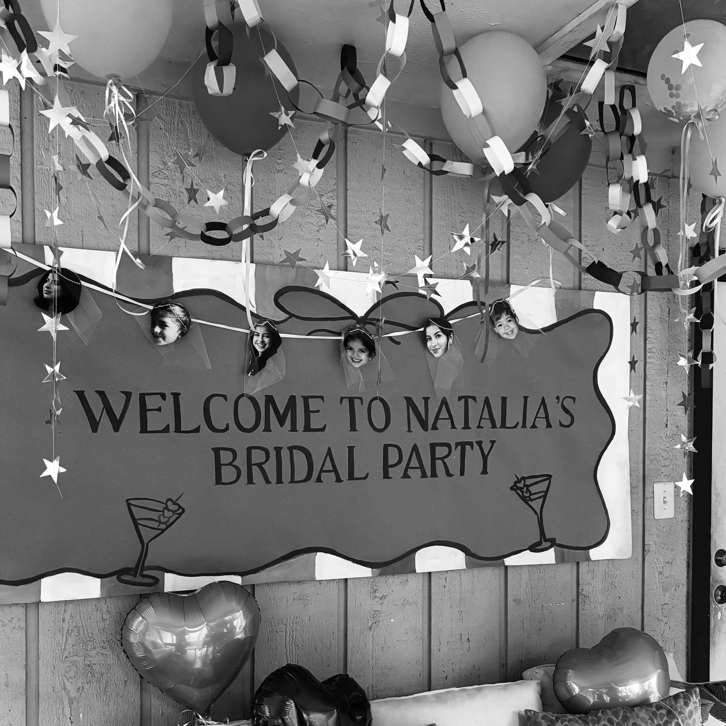 Decorations for a bridal party including balloons, star-shaped hanging decorations, paper chains, and cutouts of children's faces, with a banner that partially reads "Welcome to Natalia's Bridal Party".