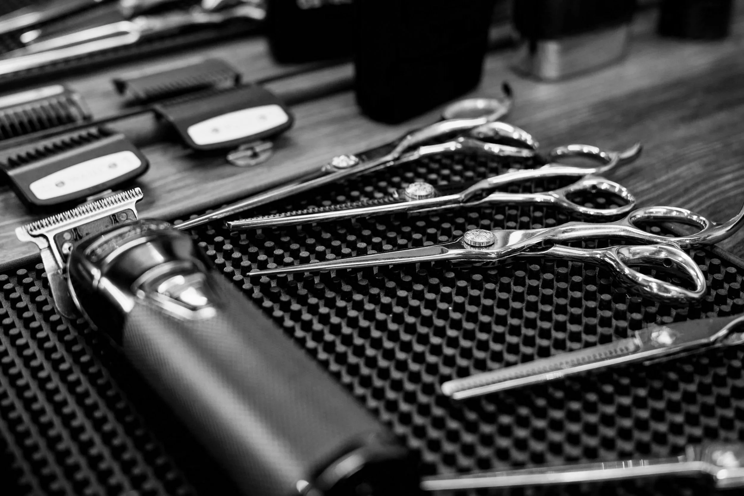 Schere, Rasierer und Klips auf einer schwarzen Gummimatte, vermutlich in einem Friseursalon oder Barbershop.