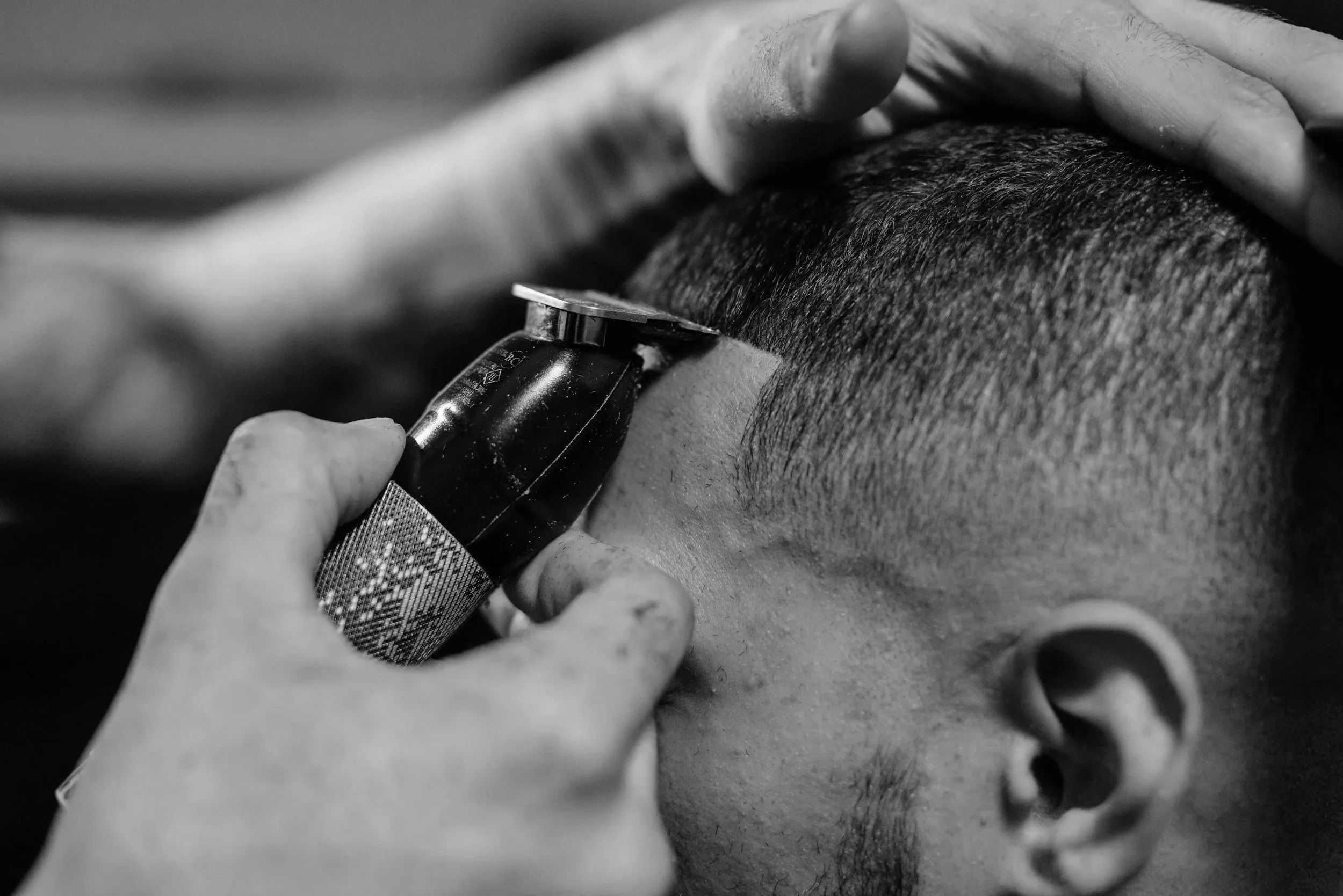Nahaufnahme eines Friseurs, der mit einem Rasiermesser die Kopfhaut eines Kunden rasiert, schwarzweiß Aufnahme.