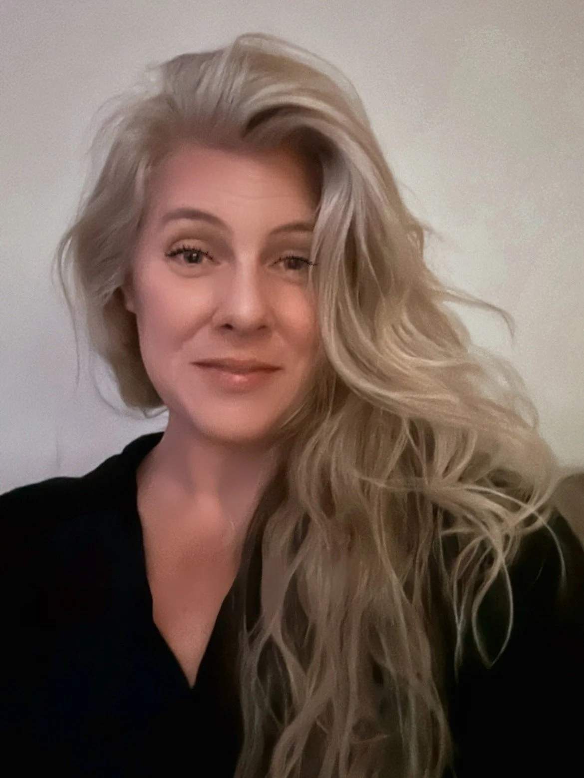 Smiling older woman with long gray hair in a living room or kitchen setting.