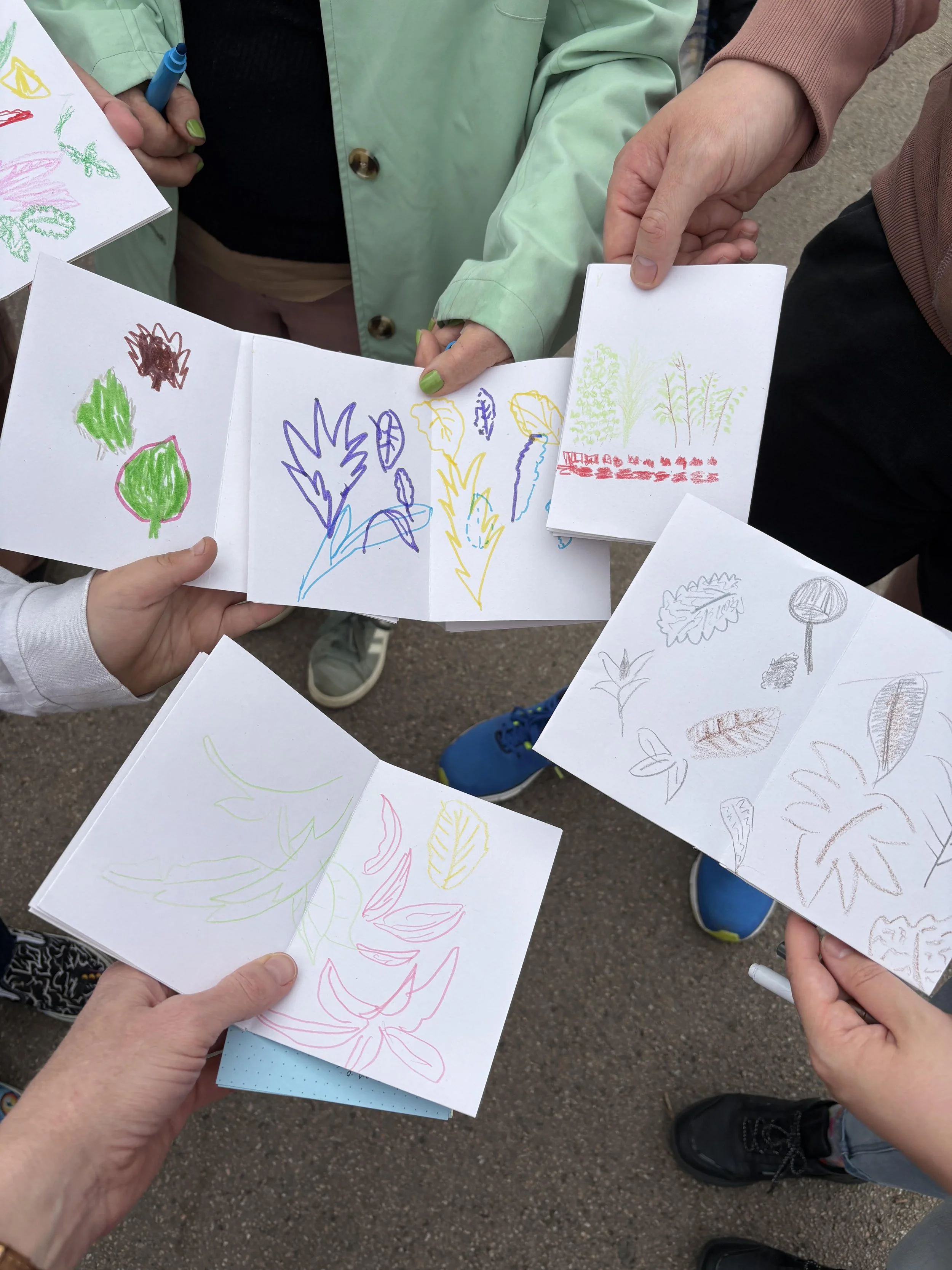 Multiple people holding and displaying various drawings of plants, leaves, and flowers on white paper.