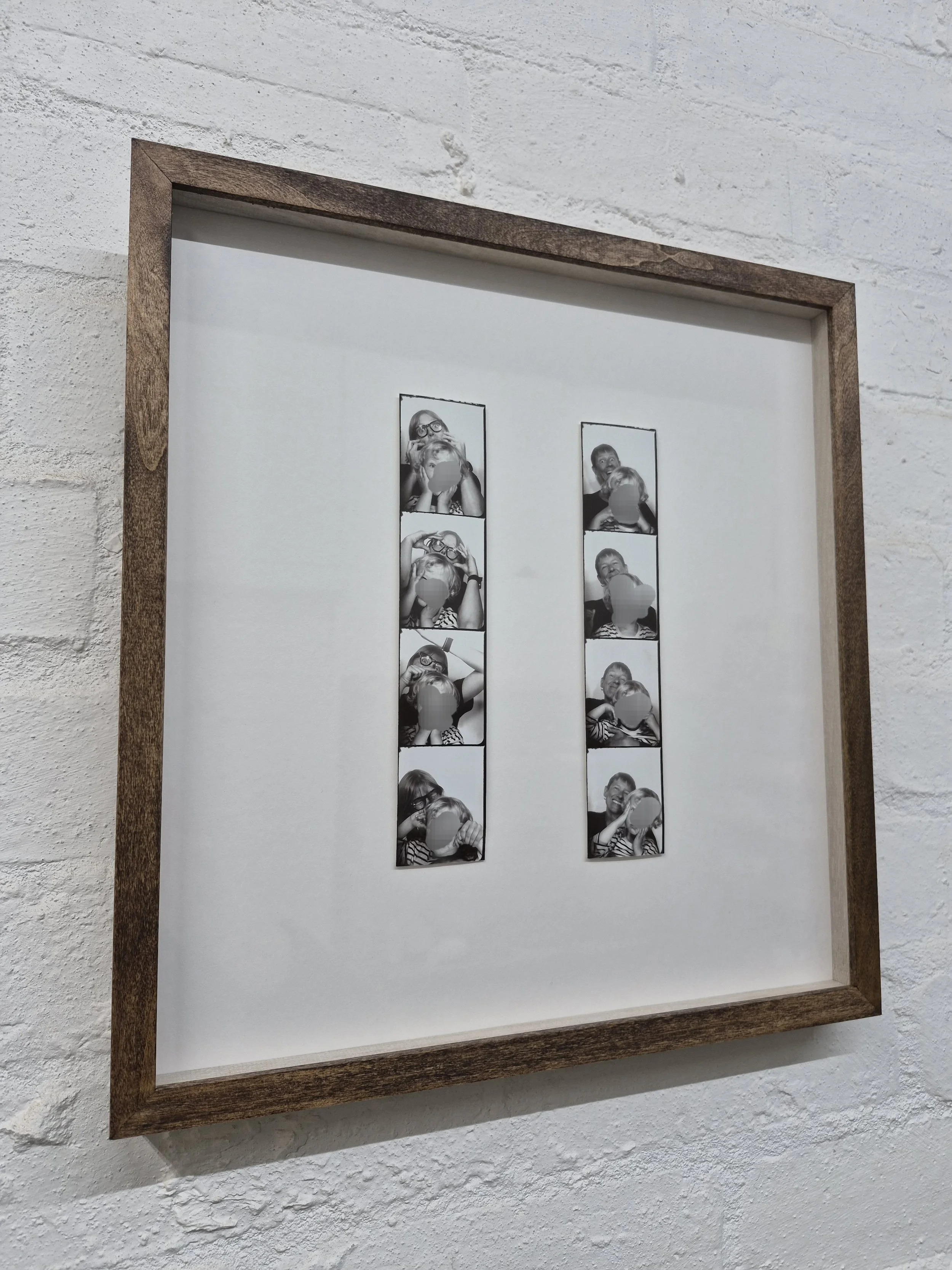 Framed collage of black and white photos of children, some with blurred faces, on a textured white wall.