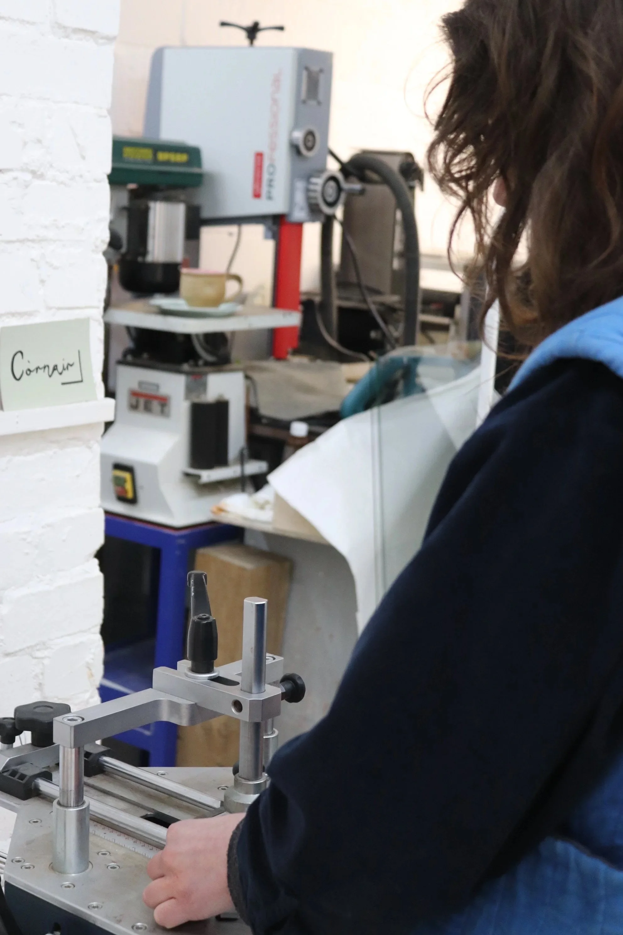 A person working with a mechanical device on a laboratory or workshop table. The device has metal rods and a sliding component. In the background, there is a machine with a cup underneath.