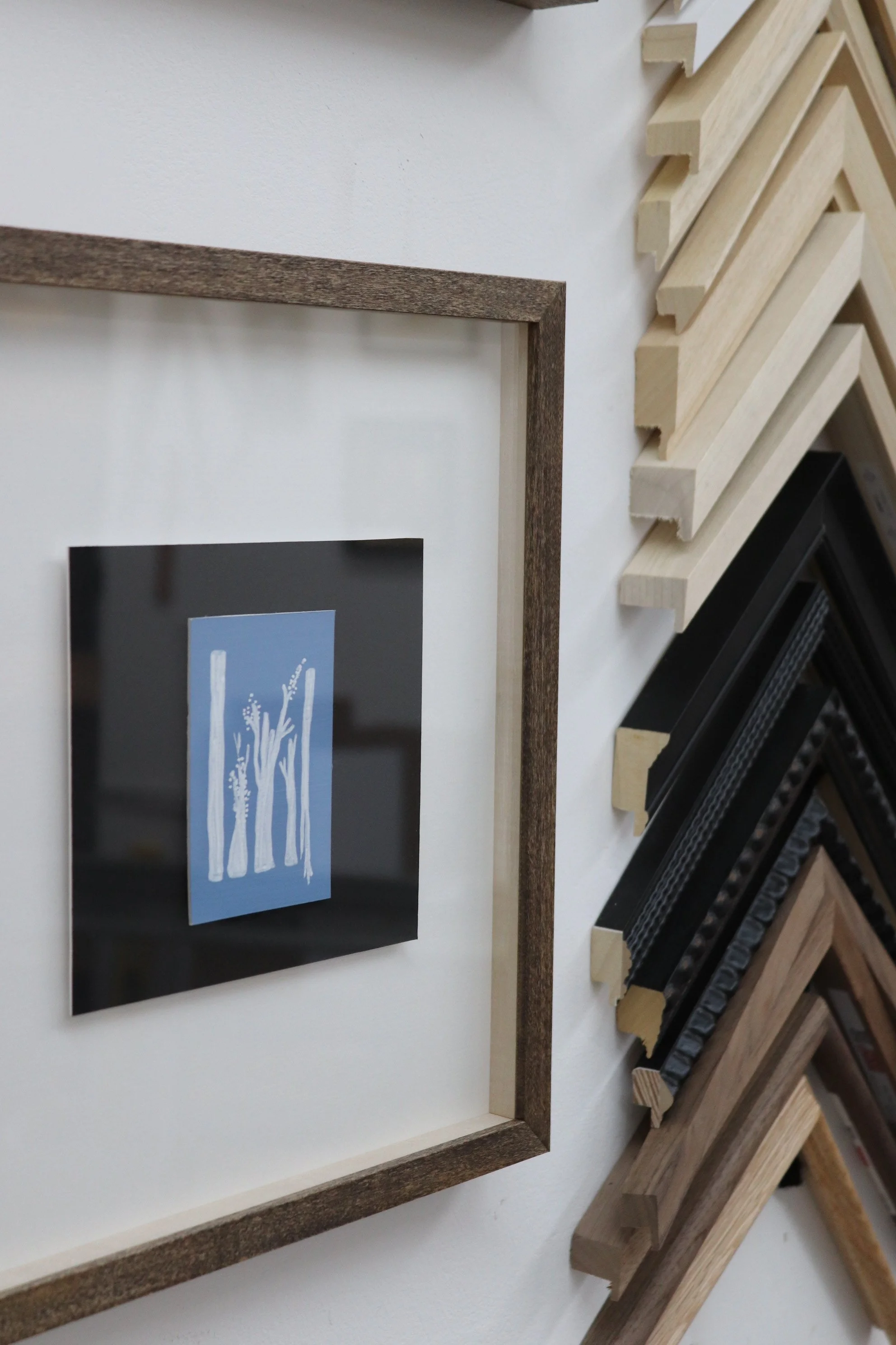 Display of various wooden picture frame samples arranged on a wall, showcasing different style and size options.