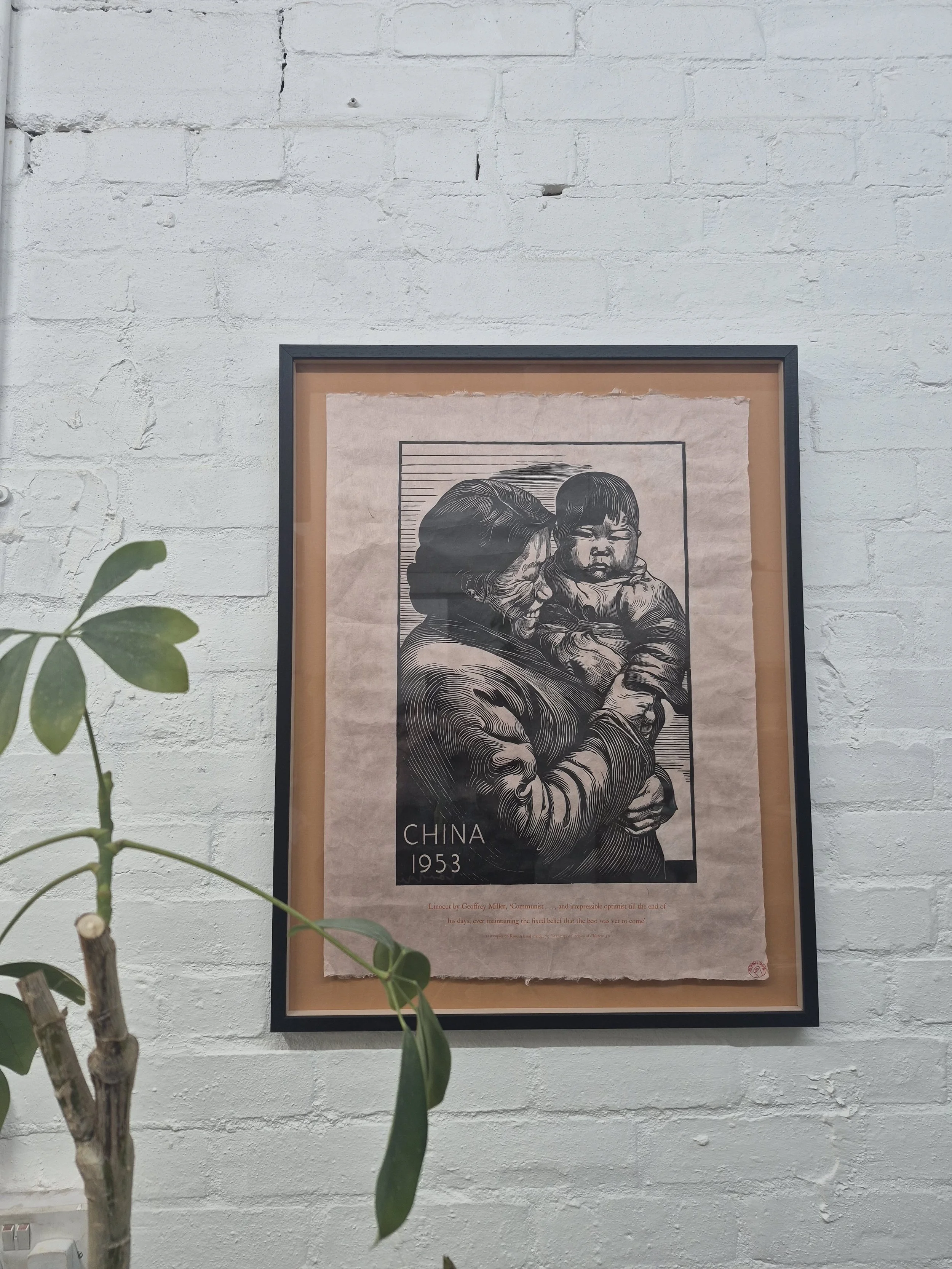 A framed black and white poster of two people hugging, with text indicating it is from China in 1953. The poster features a man and woman in an embrace, with part of the image showing a background with lines and shading. is visible in the image.