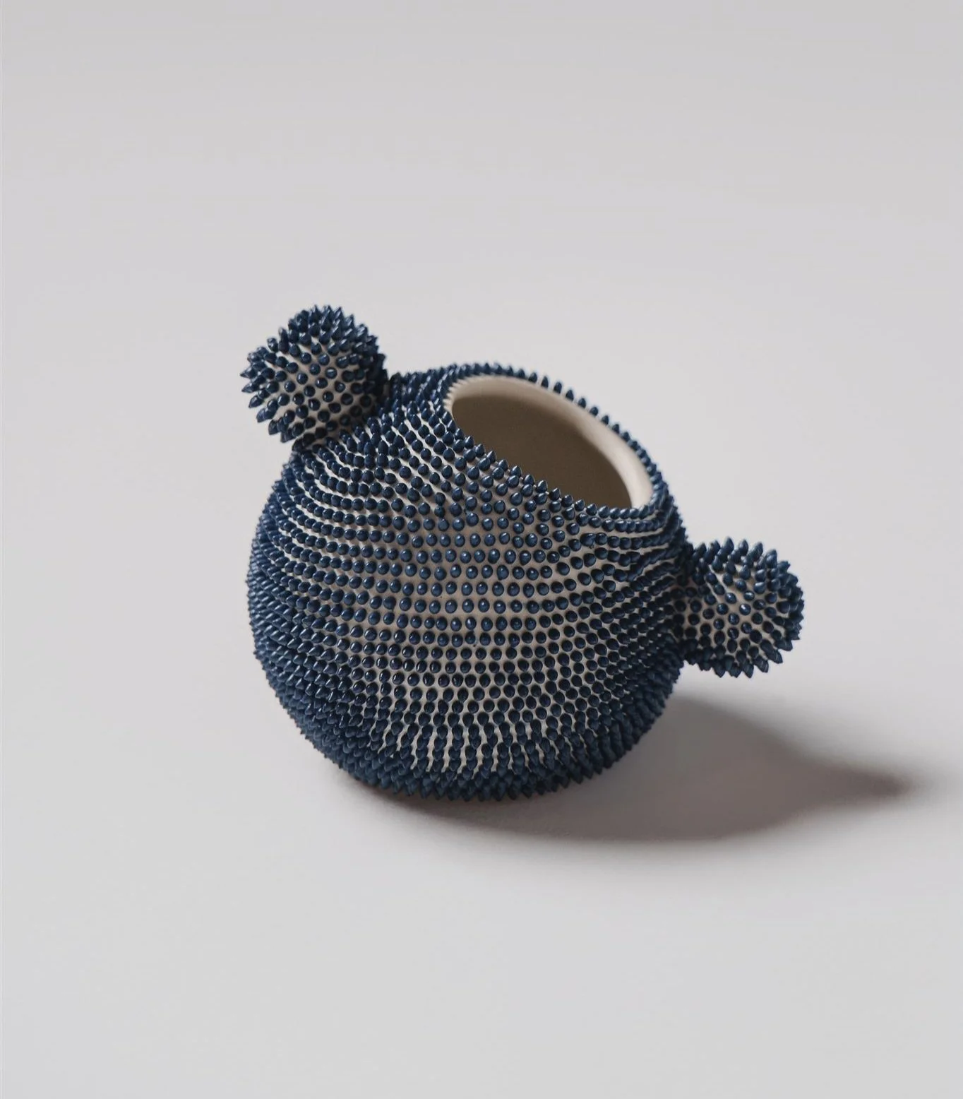 Spherical milk jug from the same tea service made of smooth white ceramic, entirely covered in small, uniform, navy-blue dots that give it a texture.