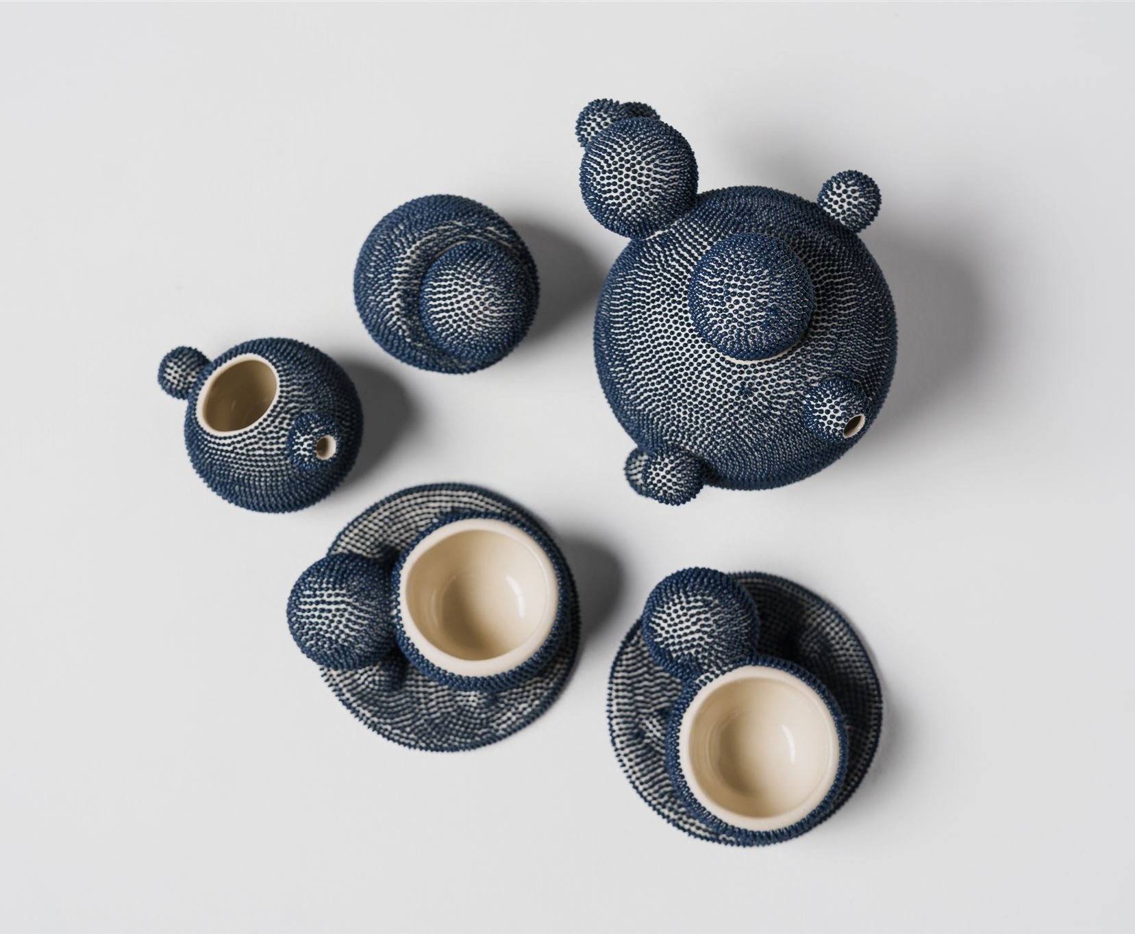 An aerial view of a contemporary ceramic tea service composed of five pieces on a white background. The surface is dotted with delicate blue reliefs.