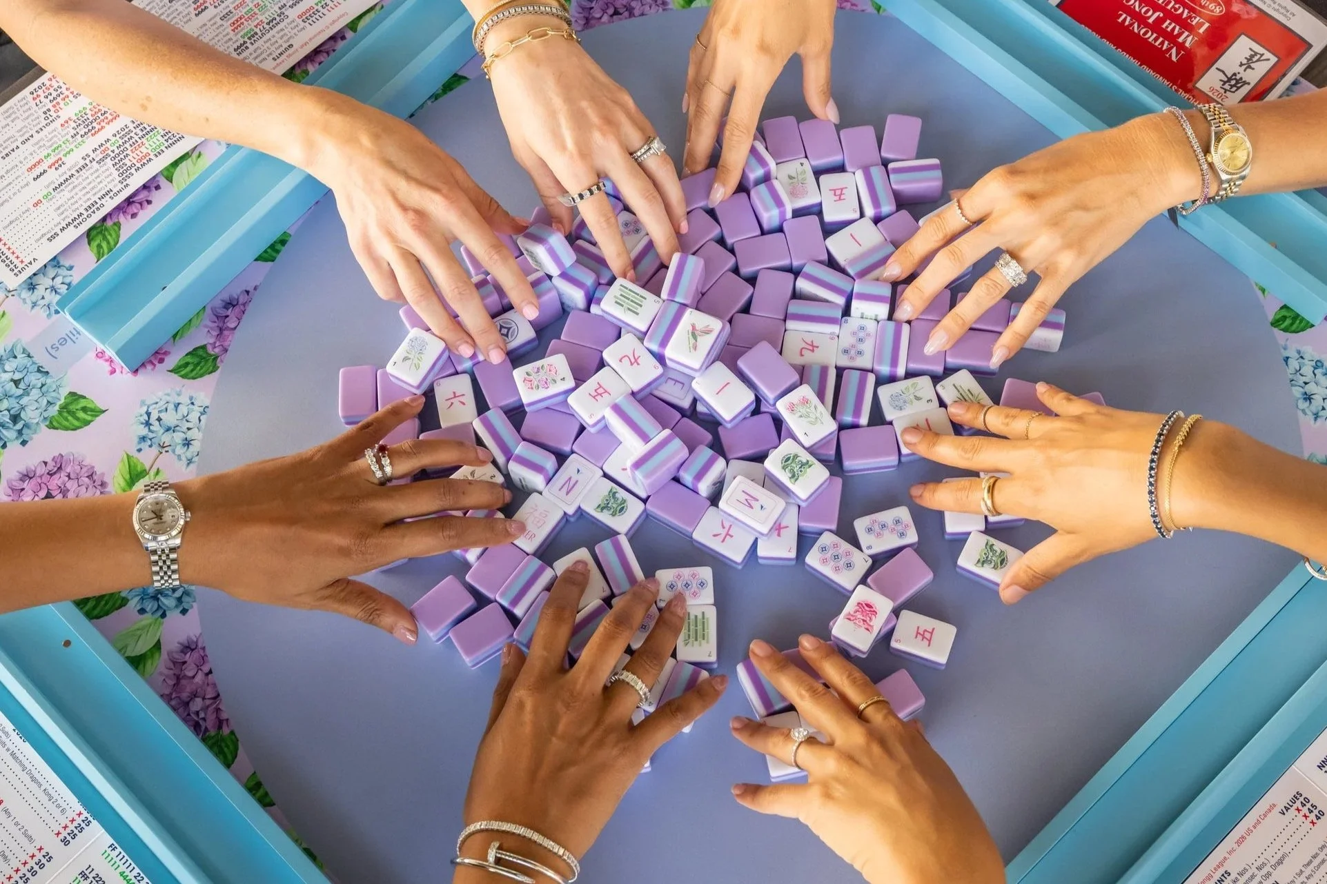 People playing mahjong with purple and white tiles with hydrangeas at a table with floral mahjong mat.