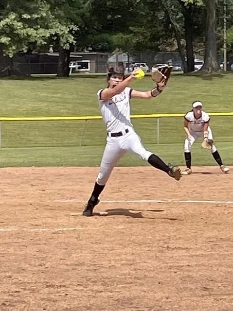 A baseball player in a white uniform making a play on a sunny field, with another player in the background.