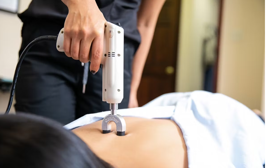 Person receiving a medical procedure with a handheld device on their abdomen in a clinical setting.