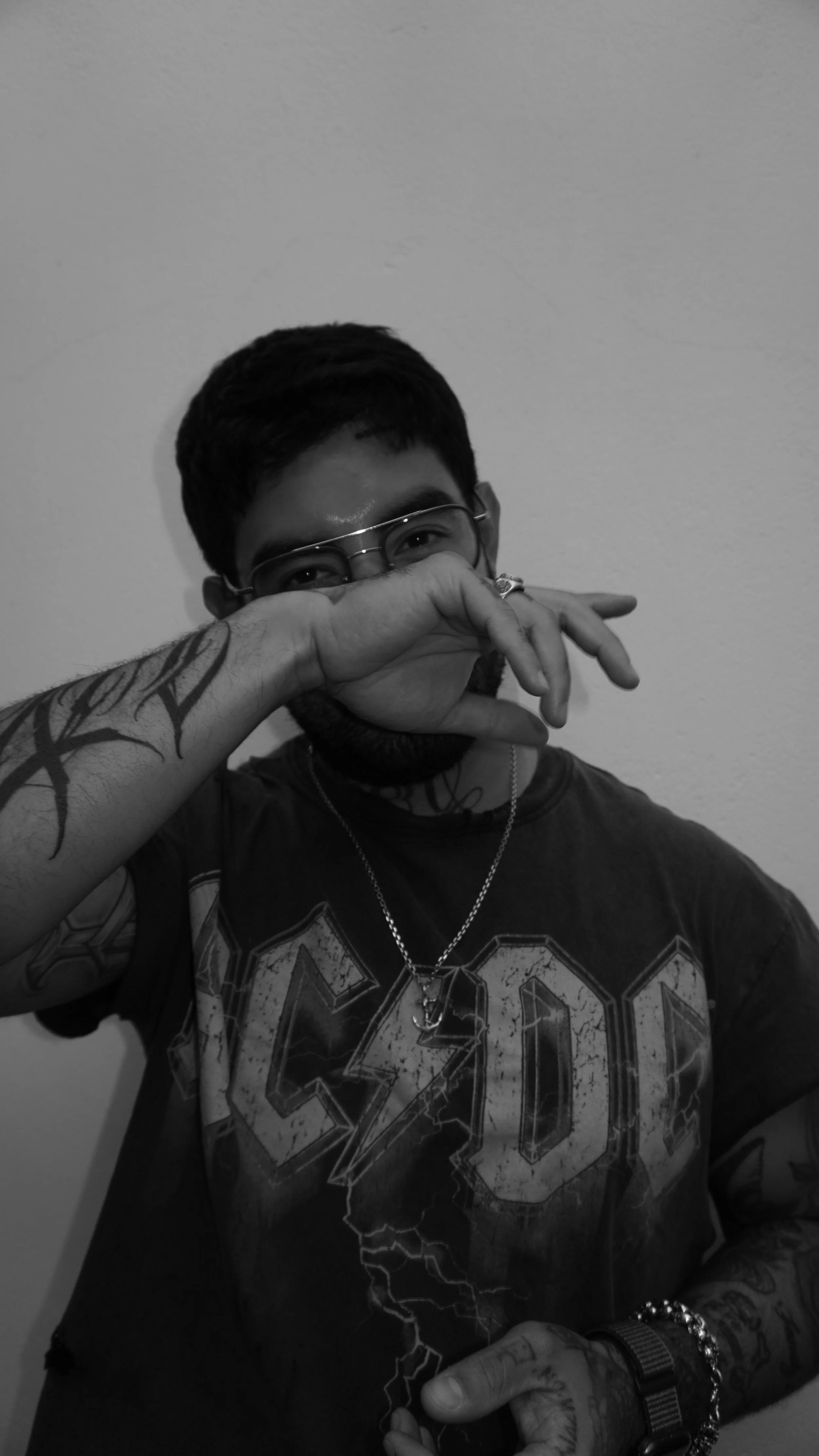 A man with glasses and tattoos covering his arm, wearing a T-shirt with a lightning design, holding a lit lighter near his face. He is smiling slightly and looking at the camera.