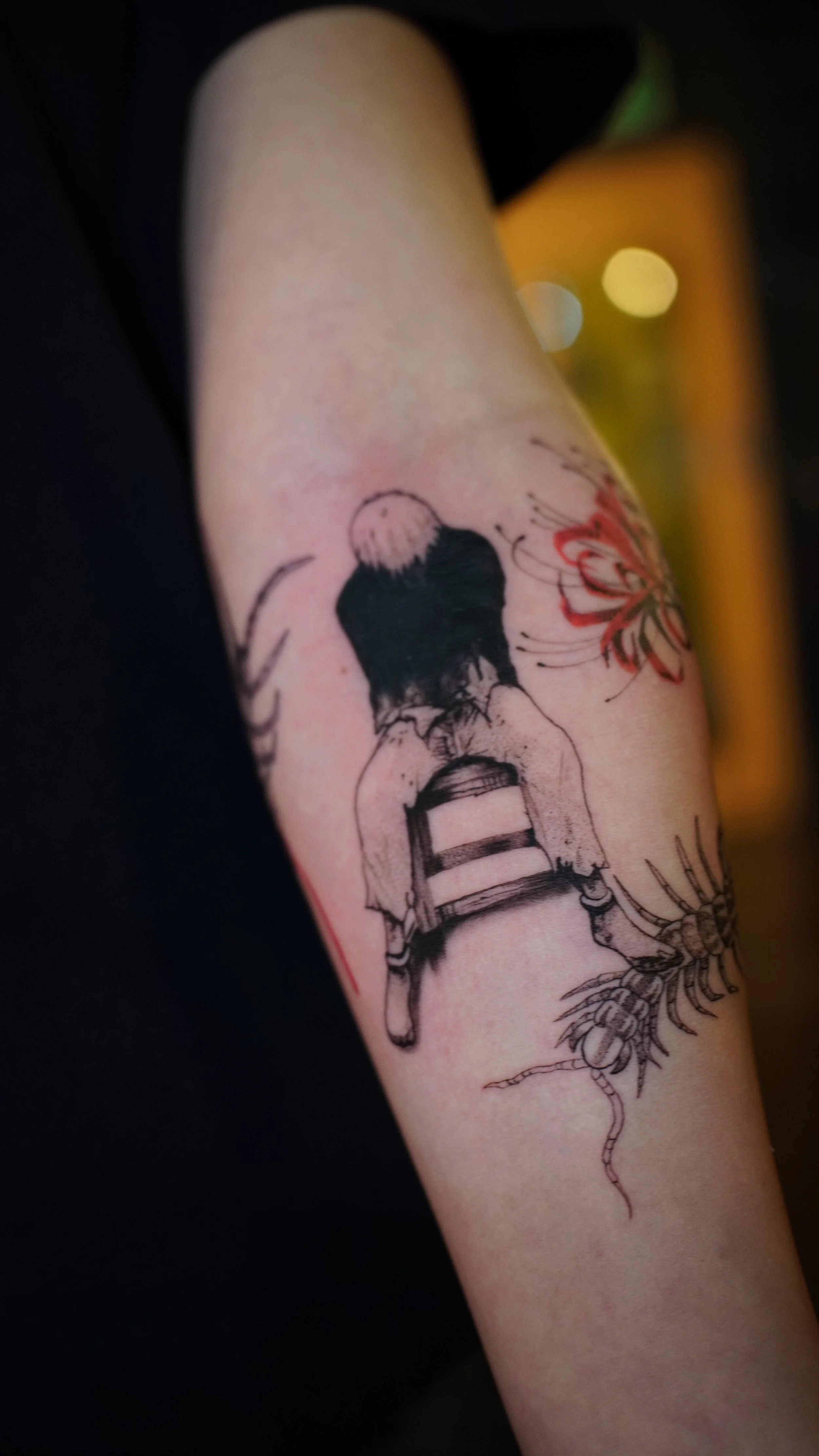 Tattoo of a woman sitting on a chair with a pumpkin and a spider in the background on a person's arm.