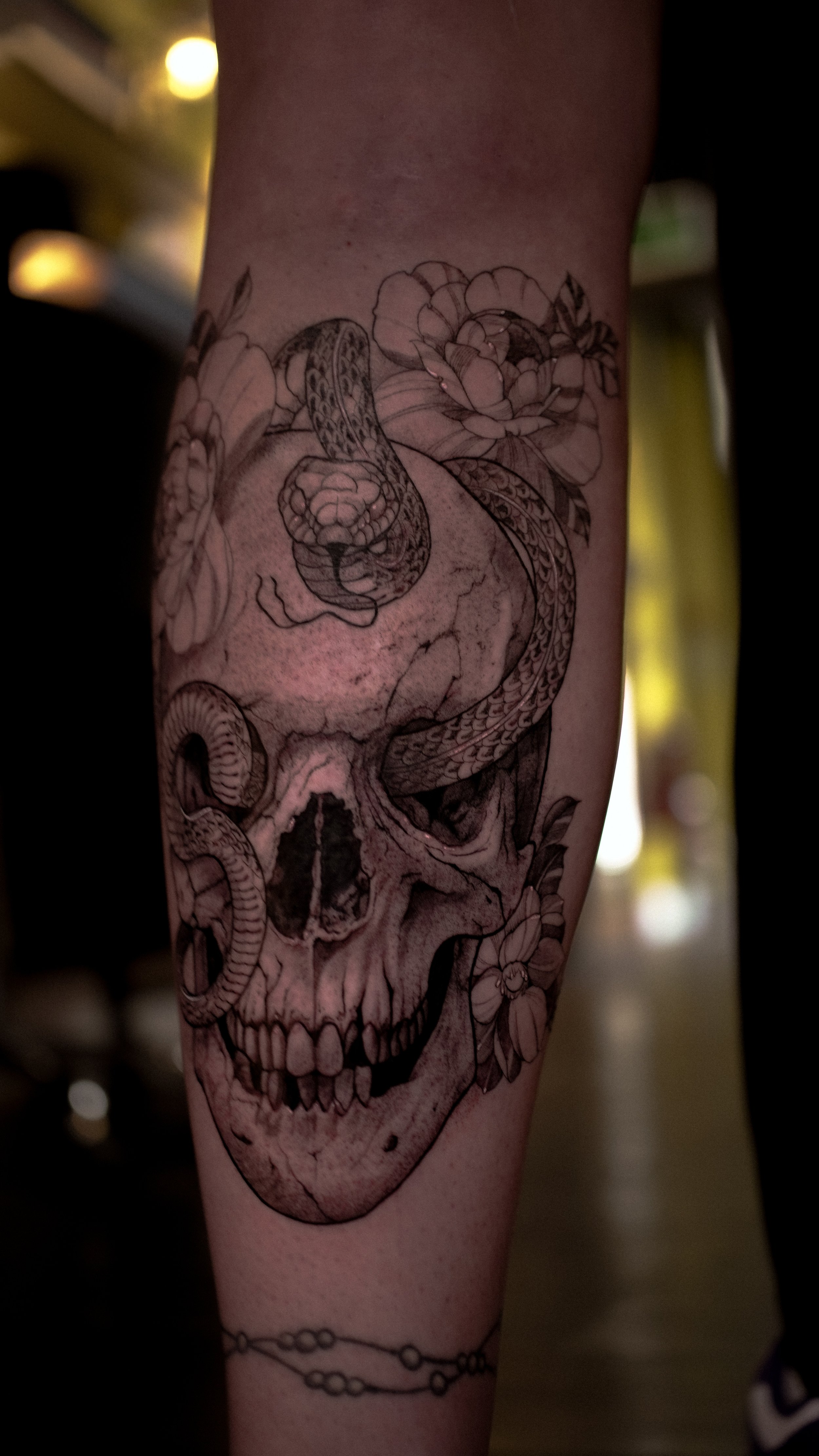 Tattoo of a human skull with a snake intertwined around it and flowers surrounding.