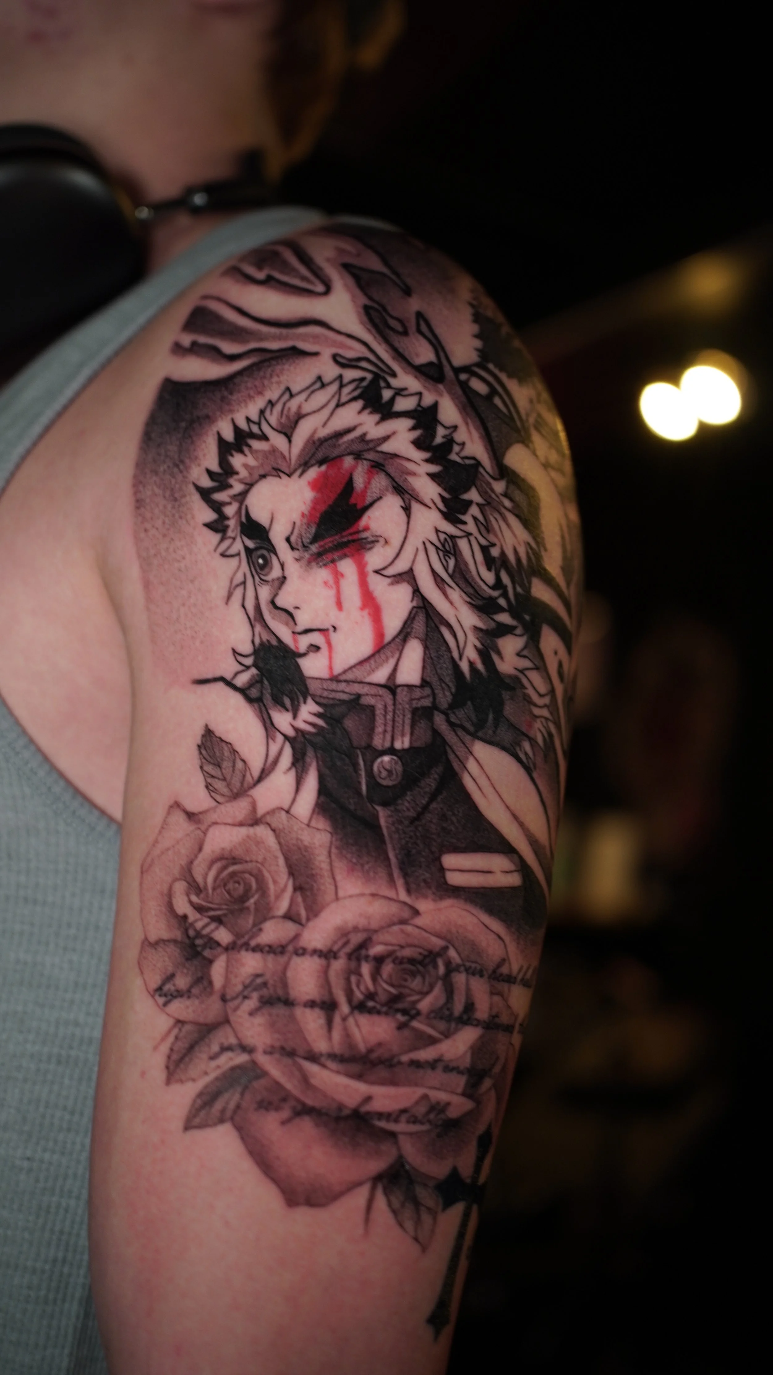 Tattoo of a woman with wolf-like features, winking, with blood streaks on her face, surrounded by roses and script.